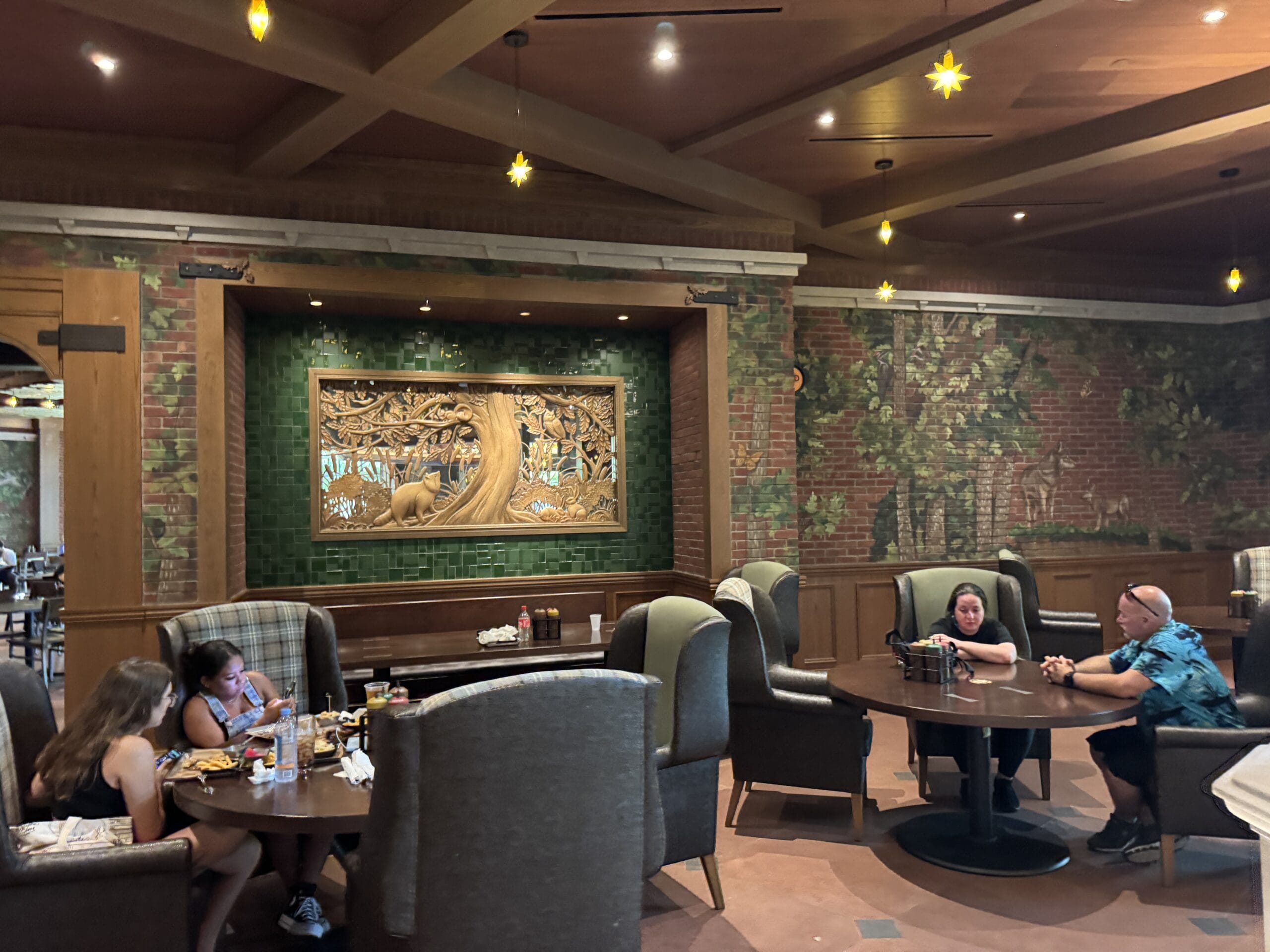 Guests enjoy meals at The Oak & Star Tavern, a warm eatery with a magical tree mural, wood ceiling, and Disney-like star lights.