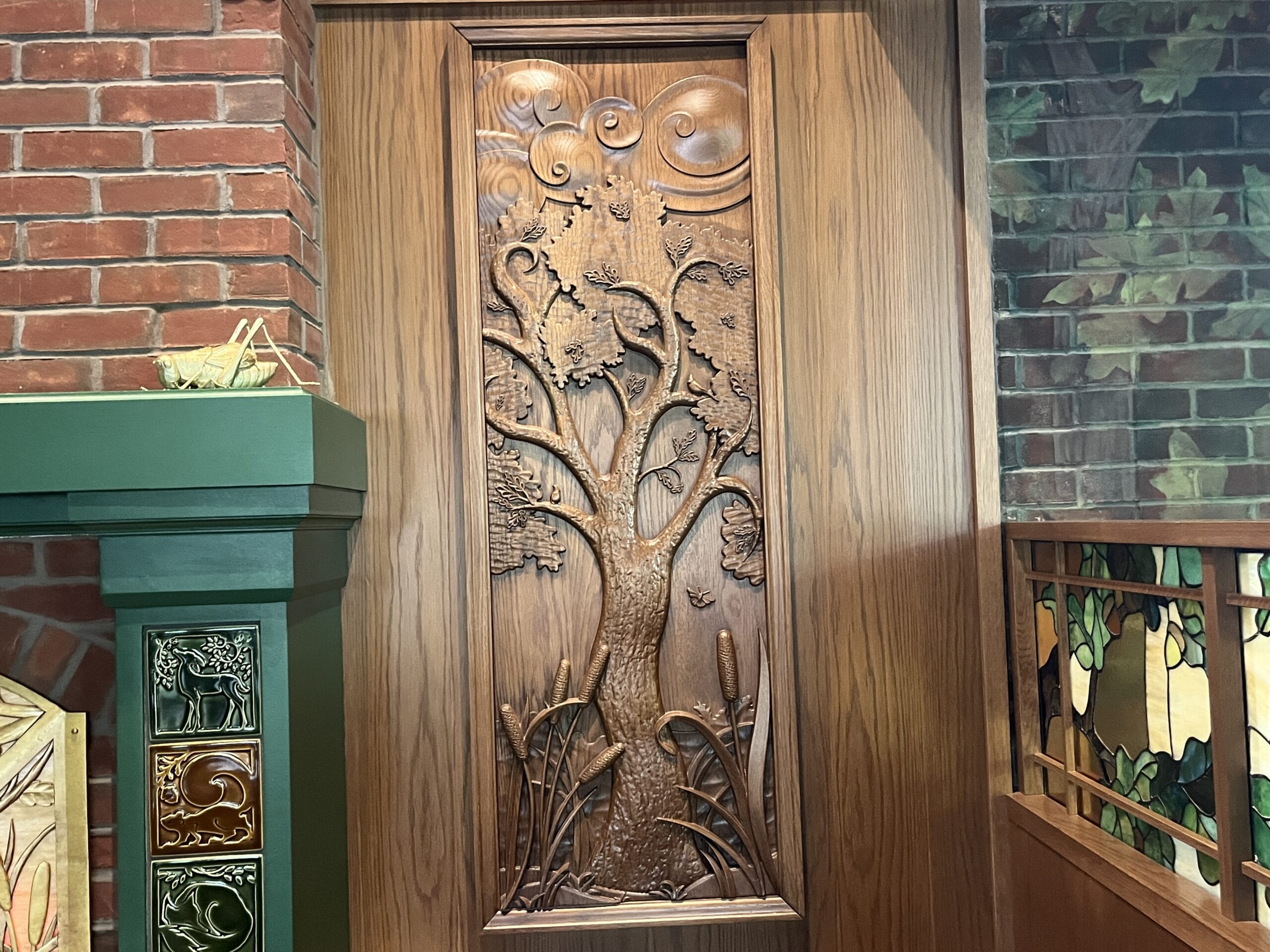 Wooden panel featuring a detailed tree scene, reminiscent of Disney park décor, bordered by wood, brick, and green tile.