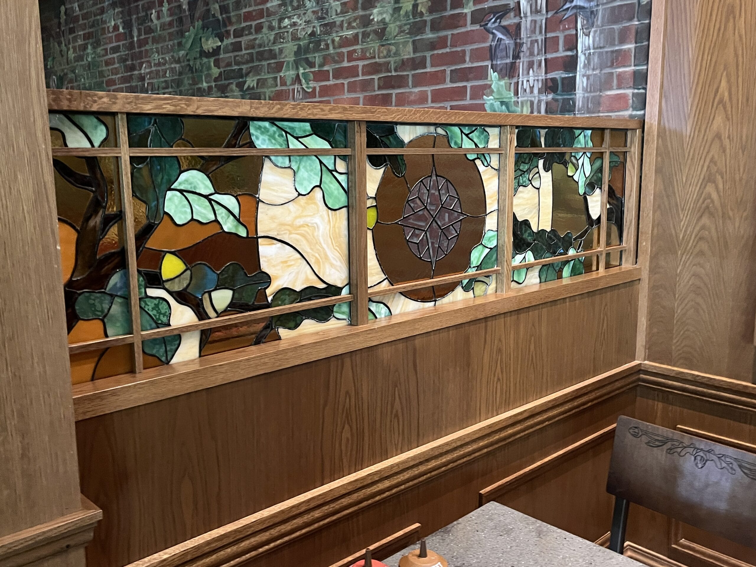 Stained glass panel with tree and leaf motif in a wooden frame at The Oak & Star Tavern, reminiscent of Fantasyland decor.