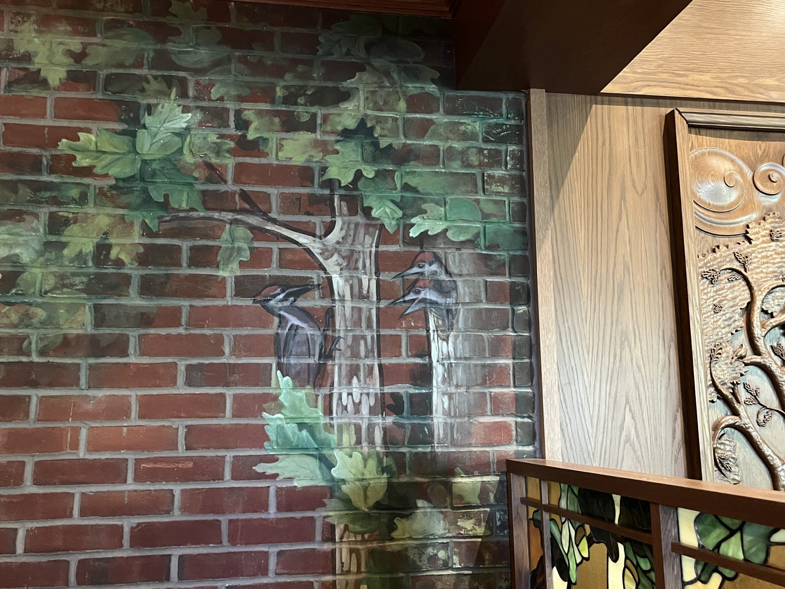 A mural of two woodpeckers on a tree decorates the red-brick wall by The Oak & Star Tavern, much like Disney’s playful park details.