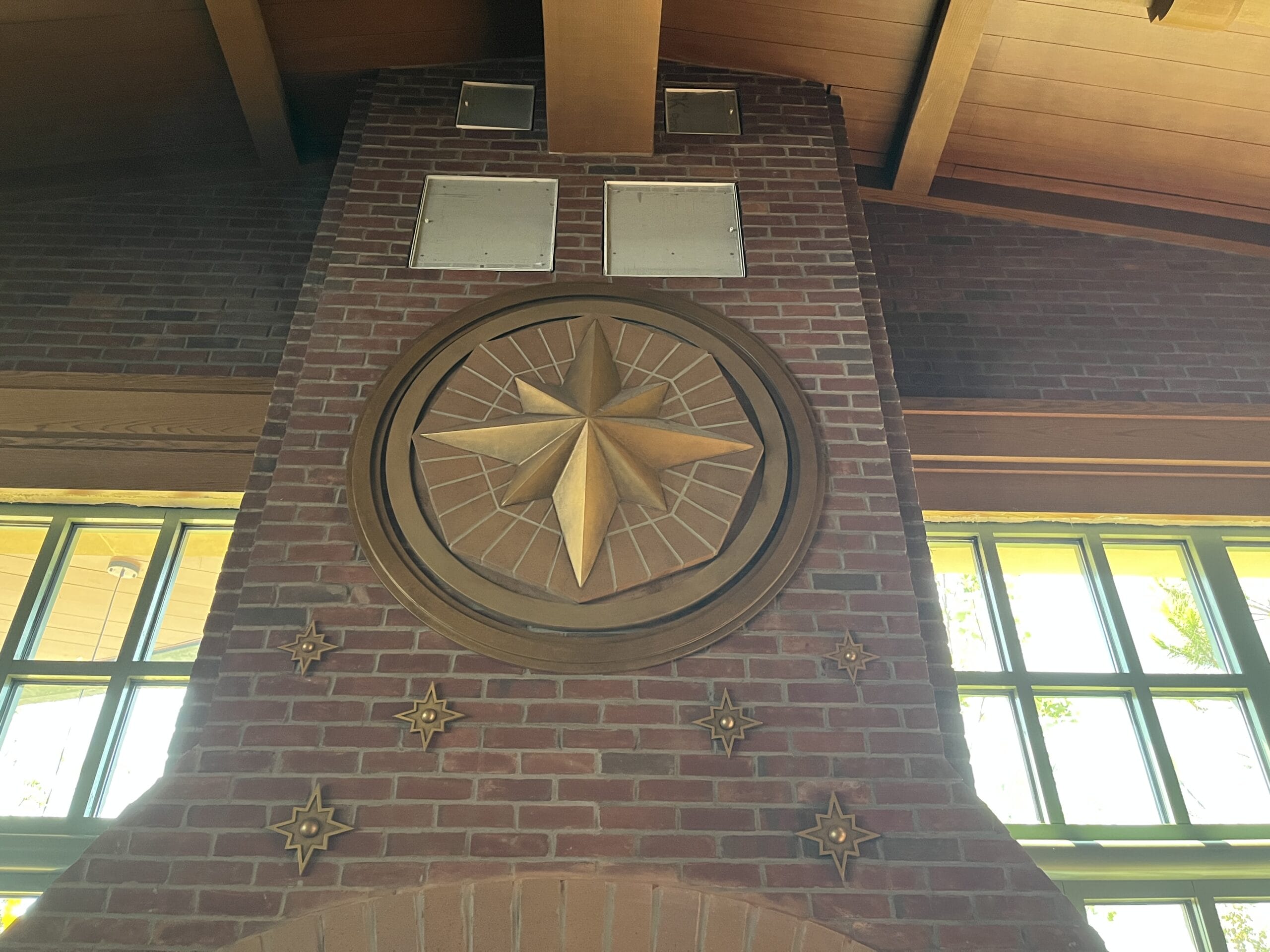 A brick wall at The Oak & Star Tavern displays a gold compass rose and stars beneath a wooden ceiling, evoking Disney park detail.