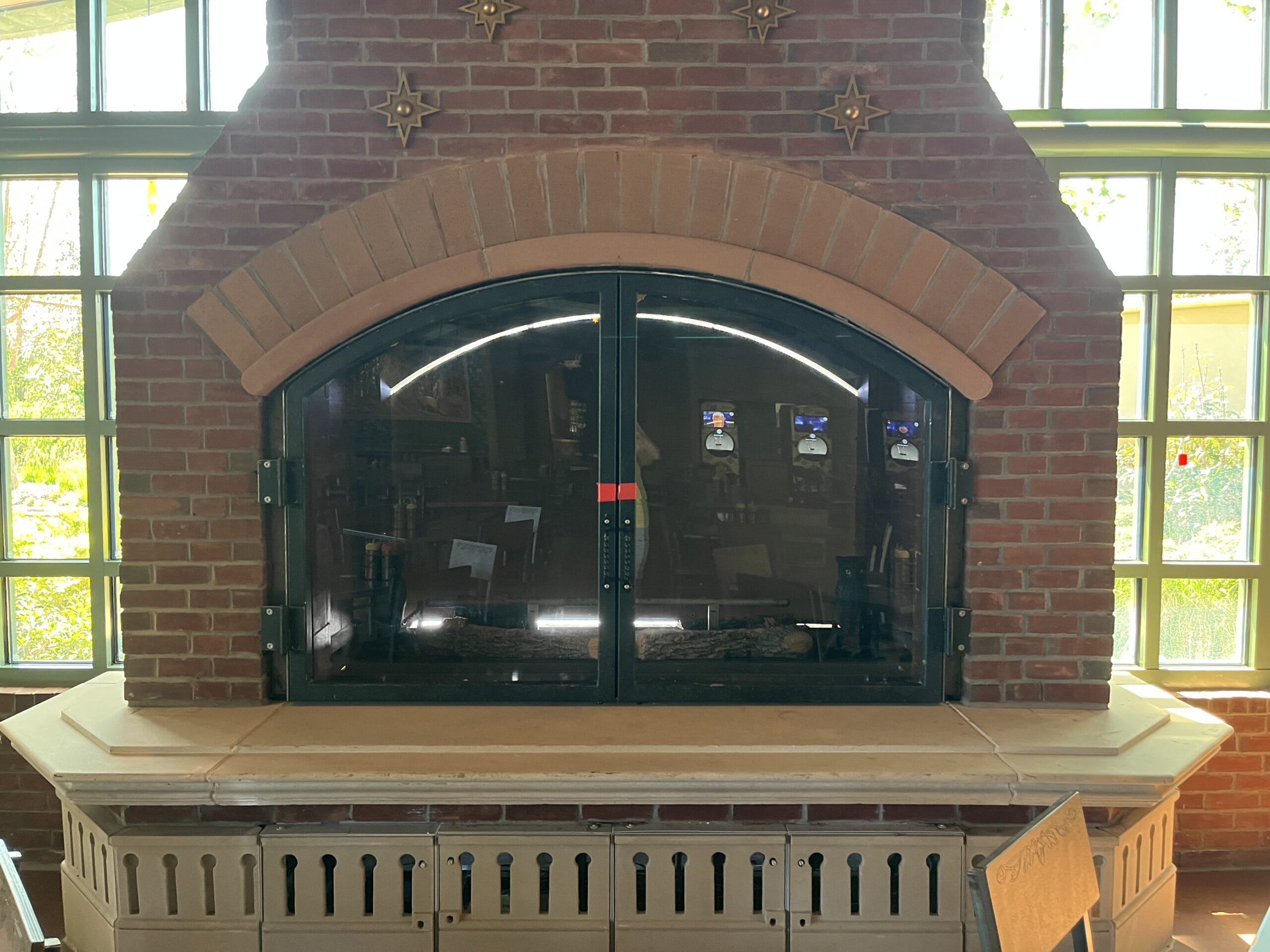 Large brick fireplace with arched glass doors, like a cozy Disney Park tavern, overlooks gardens reminiscent of EPCOT’s lush areas.