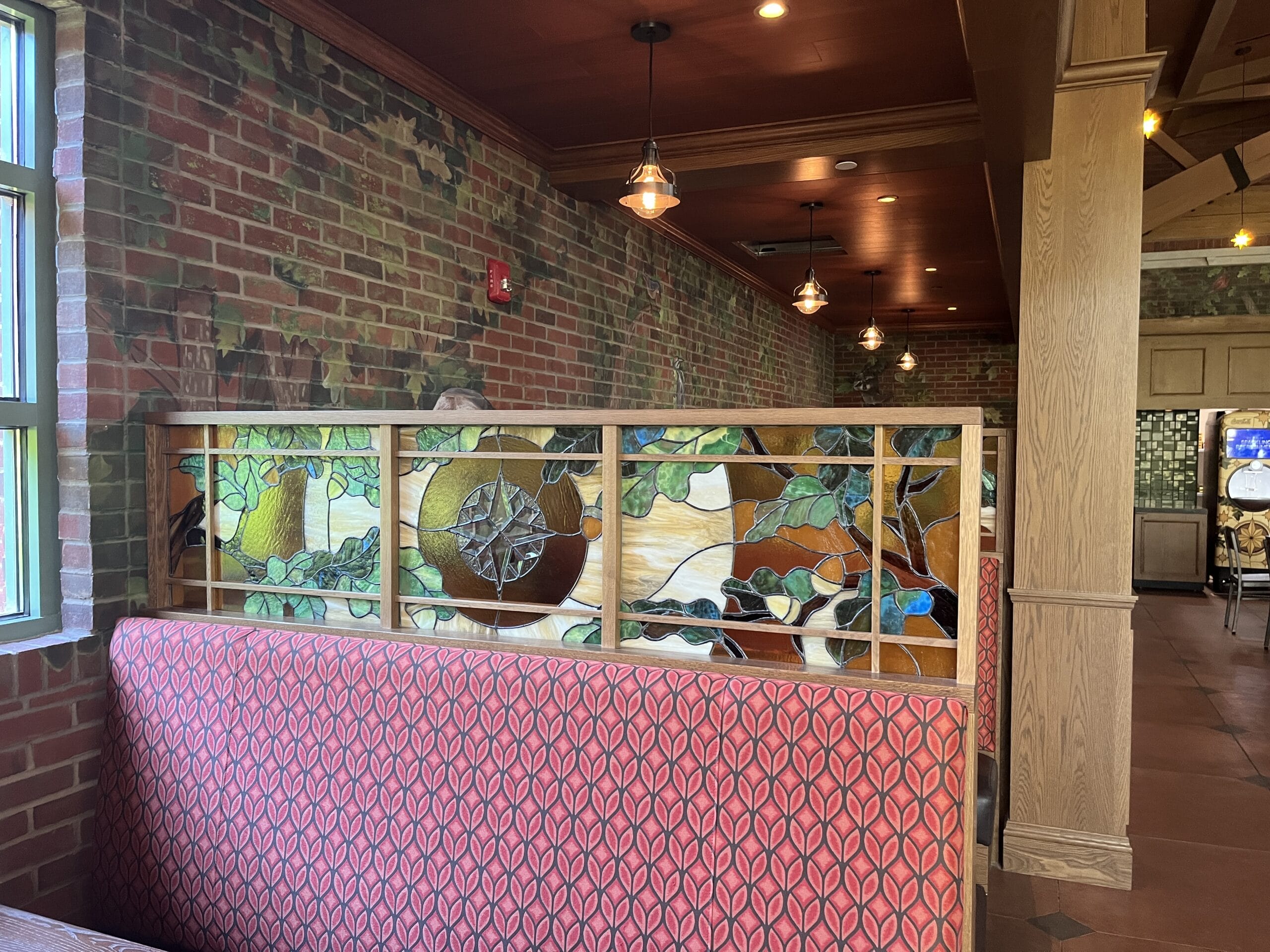 Red booth seating and a stained glass divider in The Oak & Star Tavern’s cozy, brick-walled interior—evoking Disney park tavern vibes.
