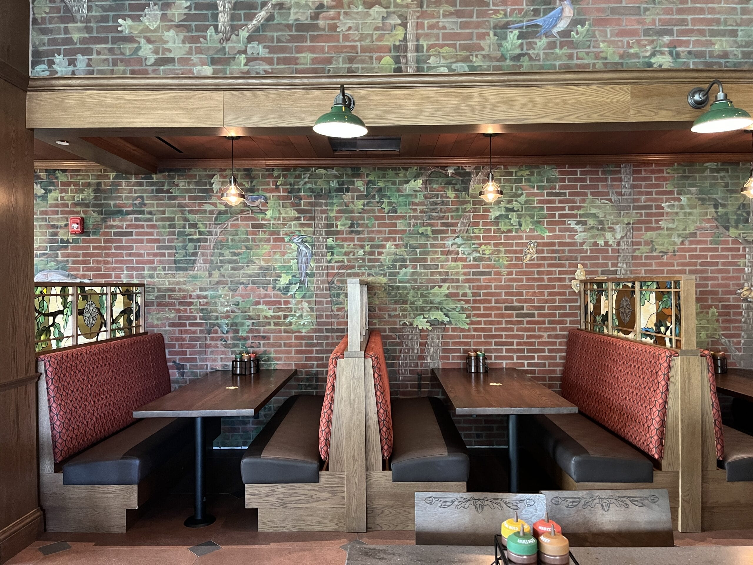 Red booths at The Oak & Star Tavern, brick walls, bird and tree mural, cozy lighting—evokes Disney park dining, no castle visible.