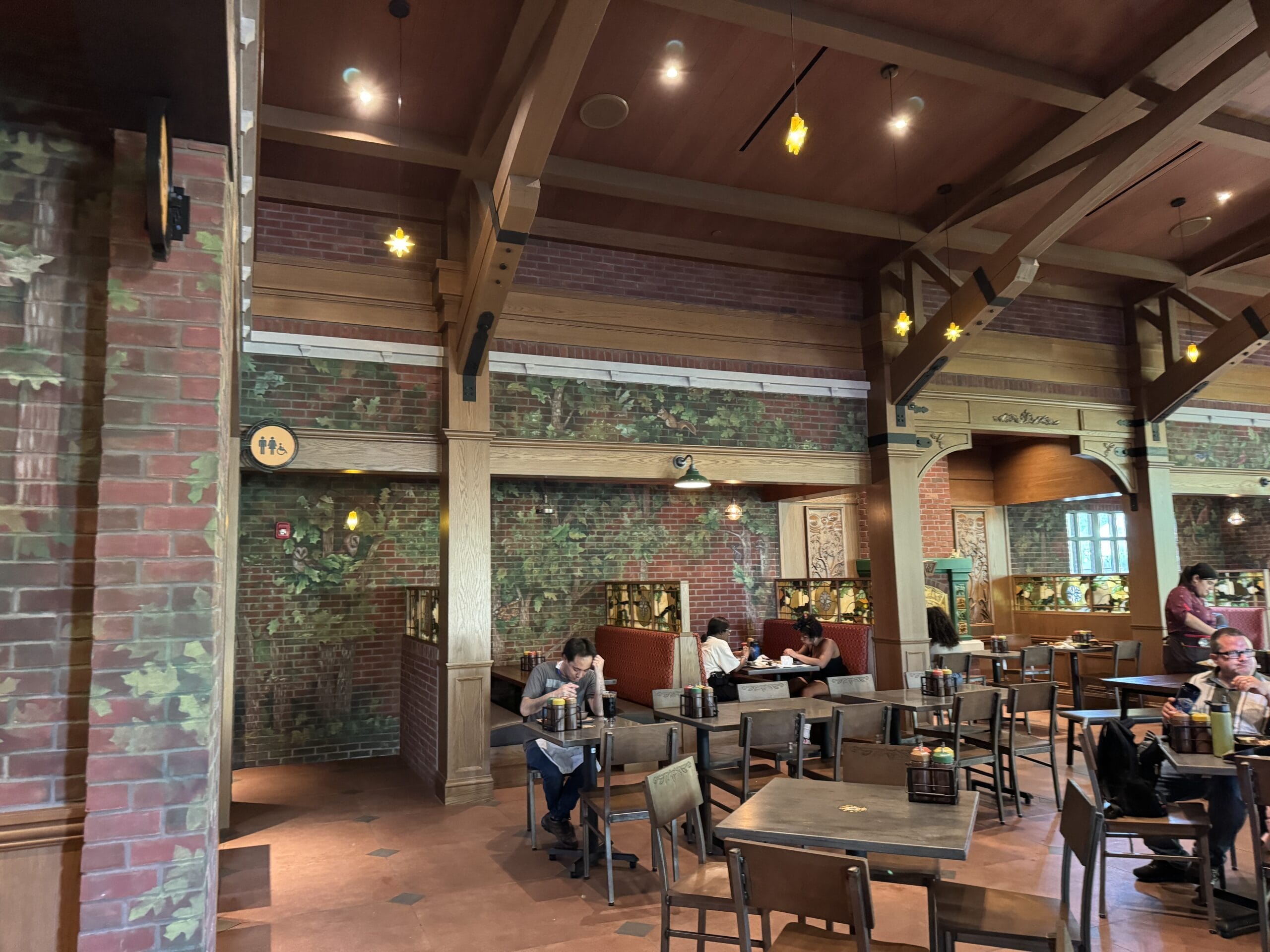 Guests gather at tables in The Oak & Star Tavern, a roomy café with brick walls, windows, and leafy murals—not unlike Main Street cafés.