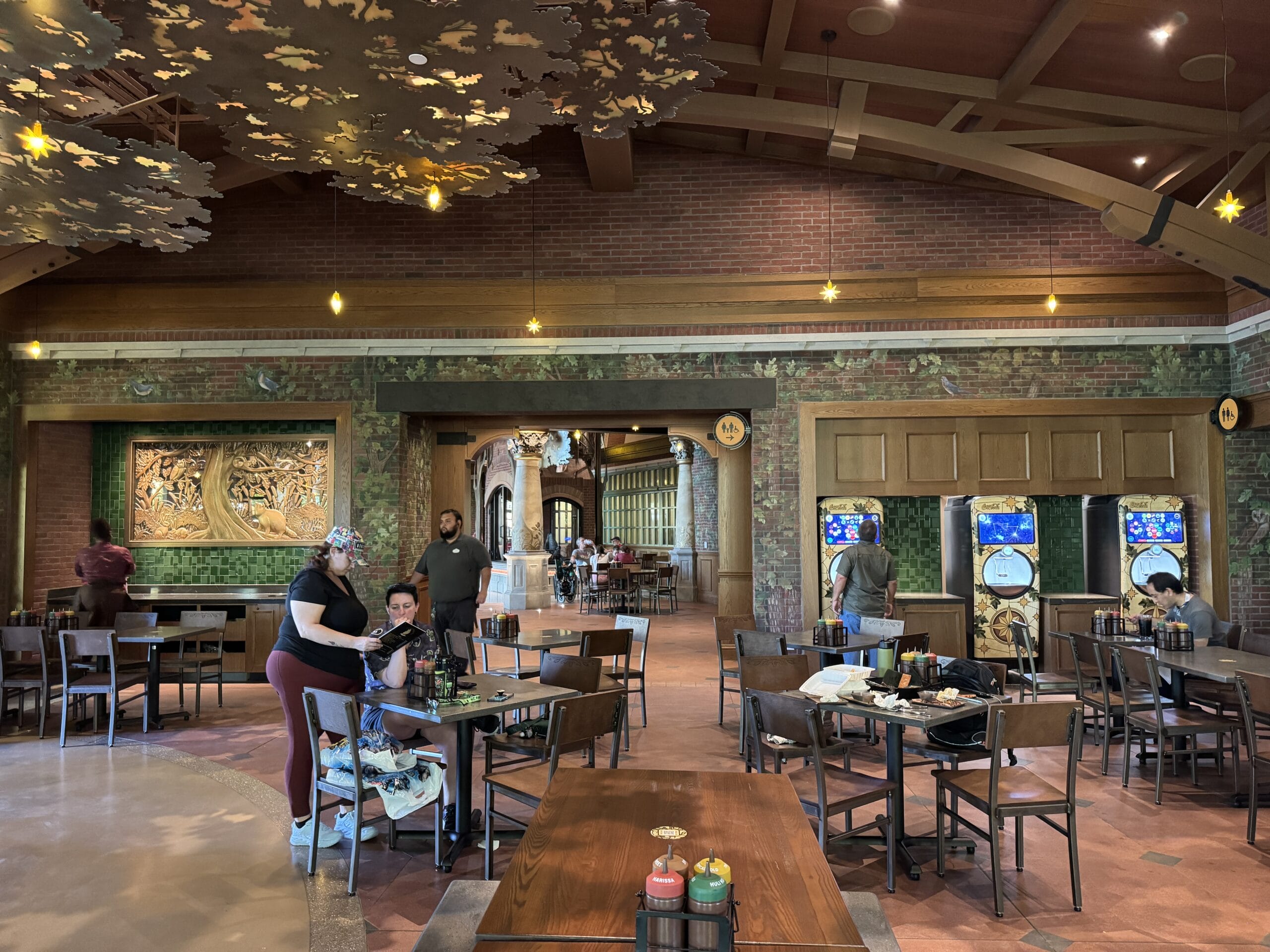 Spacious interior at The Oak & Star Tavern with wooden tables, murals, and arcade games, reminiscent of Disney park eateries.