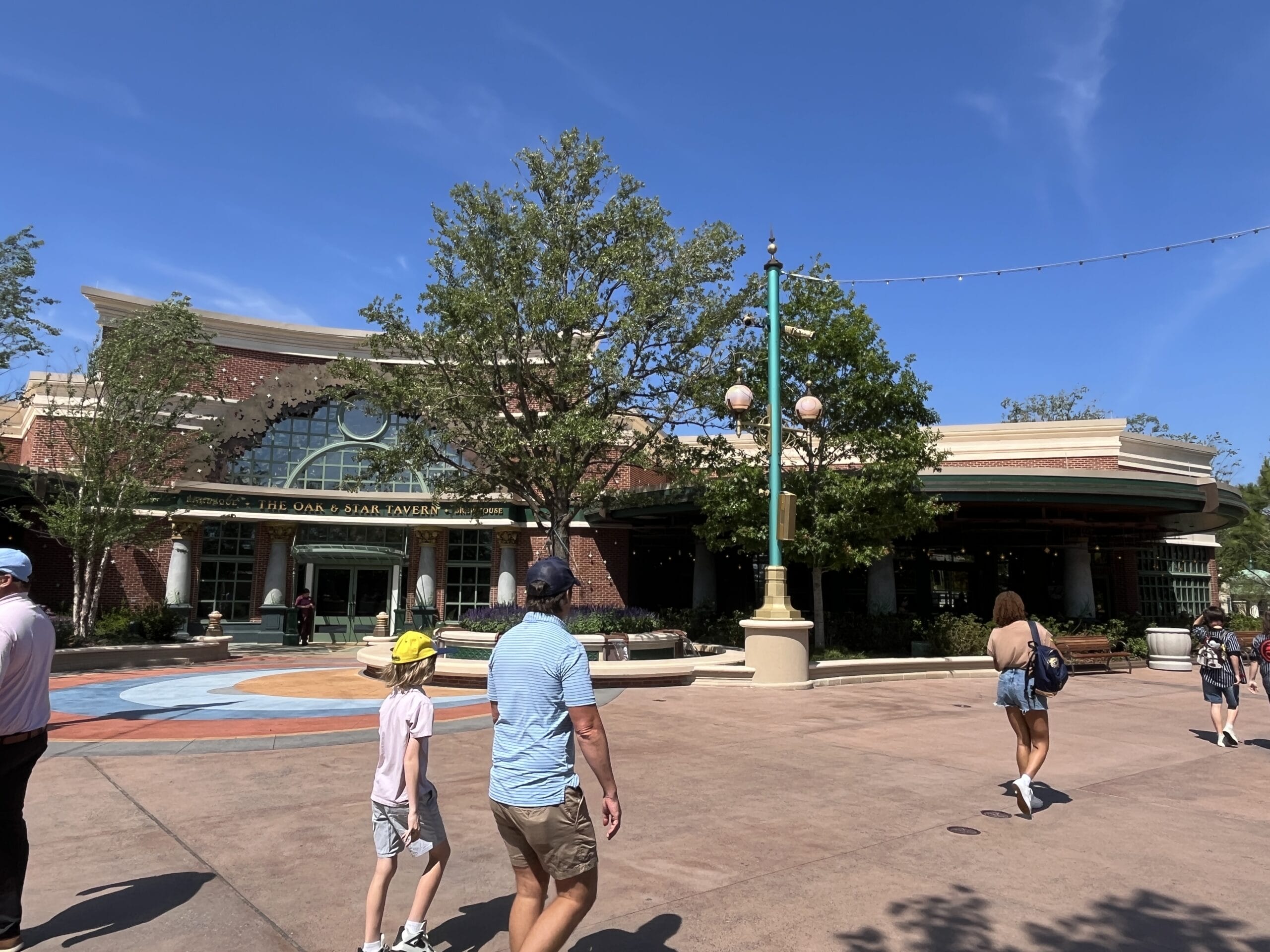 Guests walk outside The Oak & Star Tavern, a large brick building with trees and lampposts, reminiscent of Main Street U.S.A.