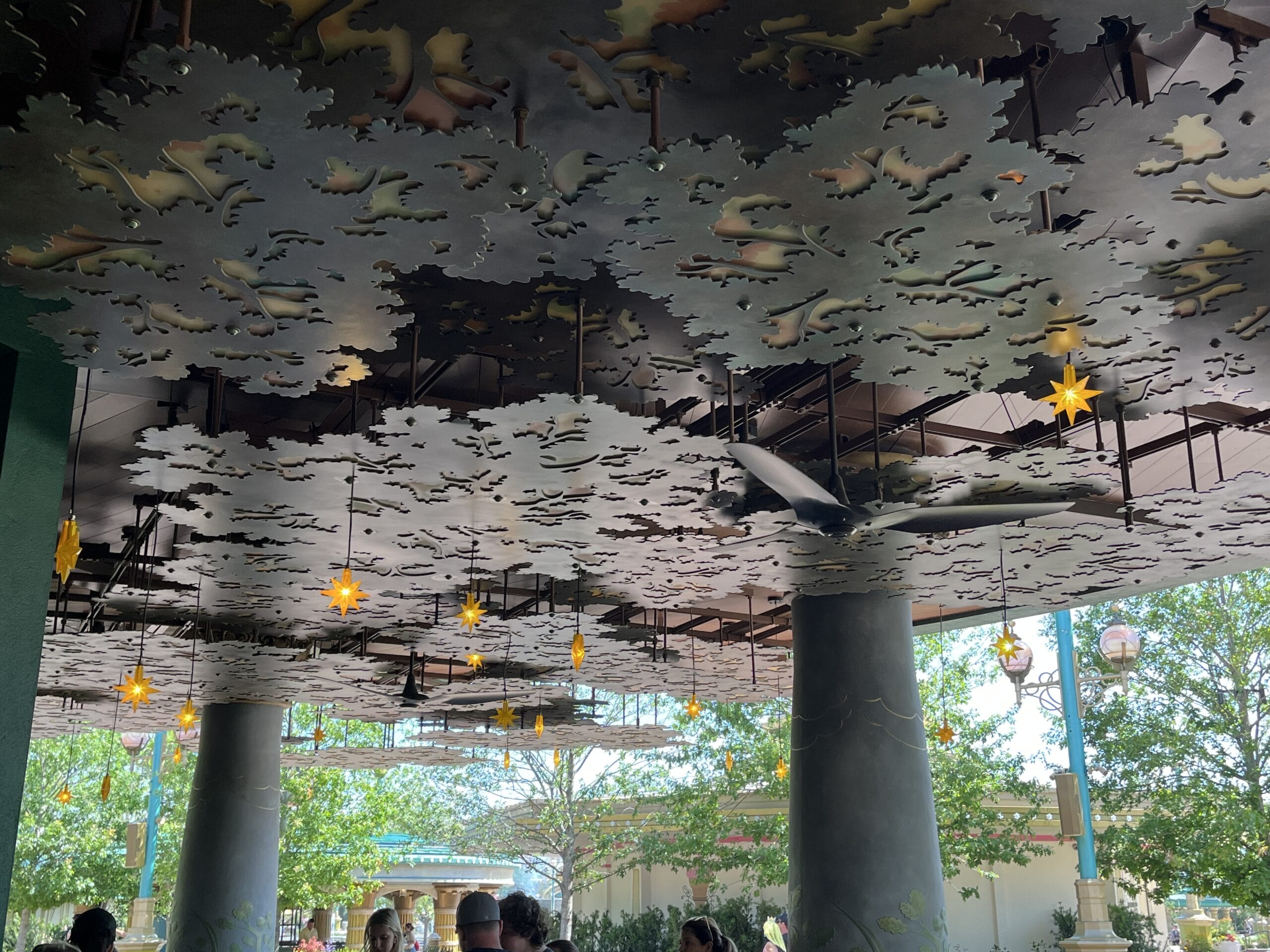 Decorative metal ceiling panels with leaf motifs and yellow star lights shine above The Oak & Star Tavern’s outdoor patio, unlike any Disney castle ceiling.