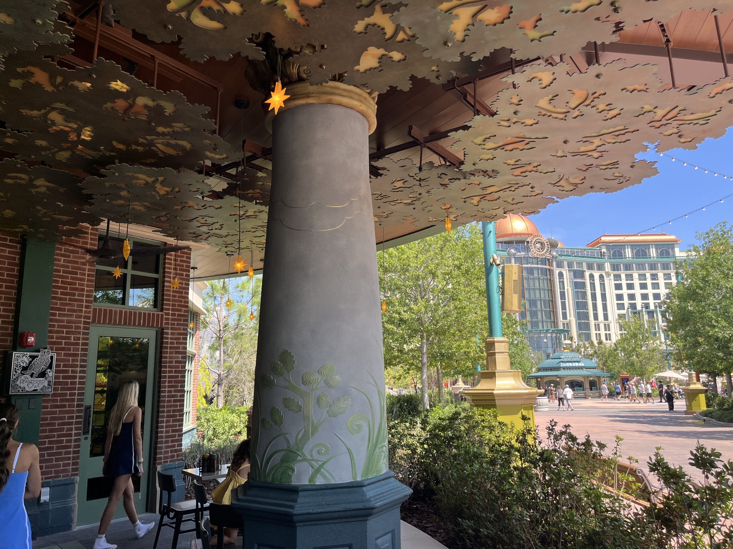 Ornate column with leafy details by The Oak & Star Tavern, beneath a canopy beside brickwork, reminiscent of Disney park theming.