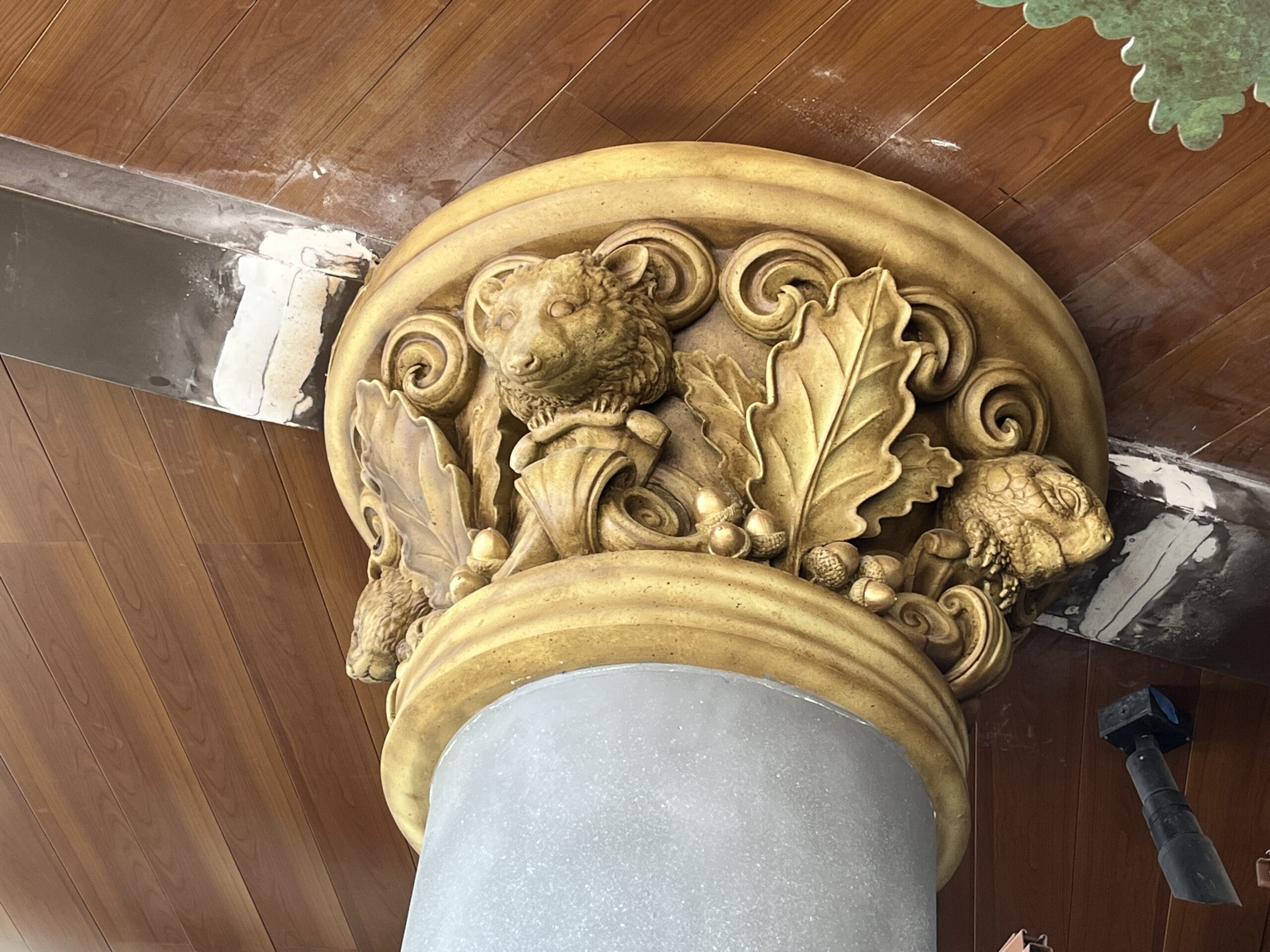 A decorative column capital at The Oak & Star Tavern, featuring gold leaves and whimsical animal faces, like Disney Park details.