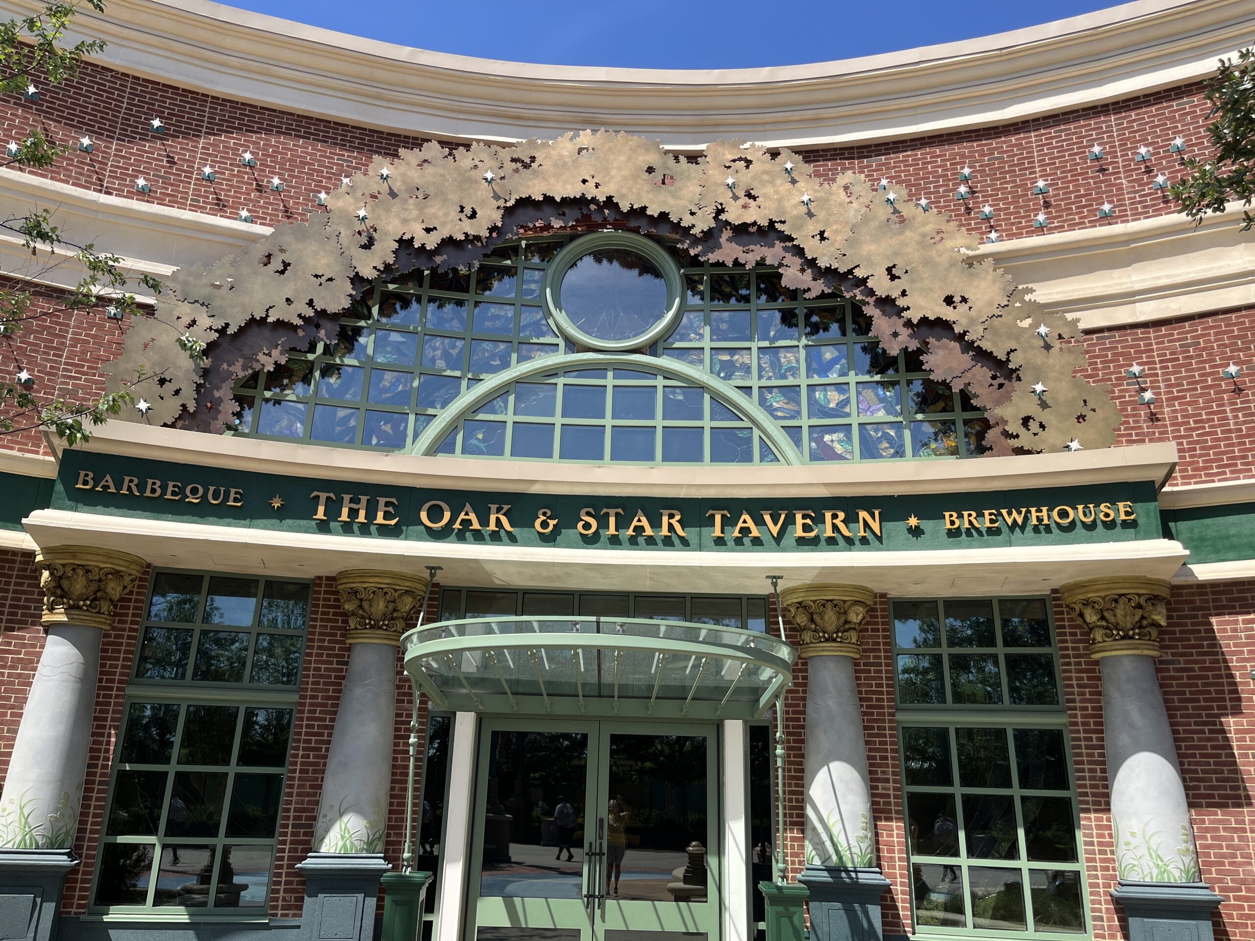 The Oak & Star Tavern’s entrance has decorative metal leaves over arched windows and columns, adding Disney park-like charm.