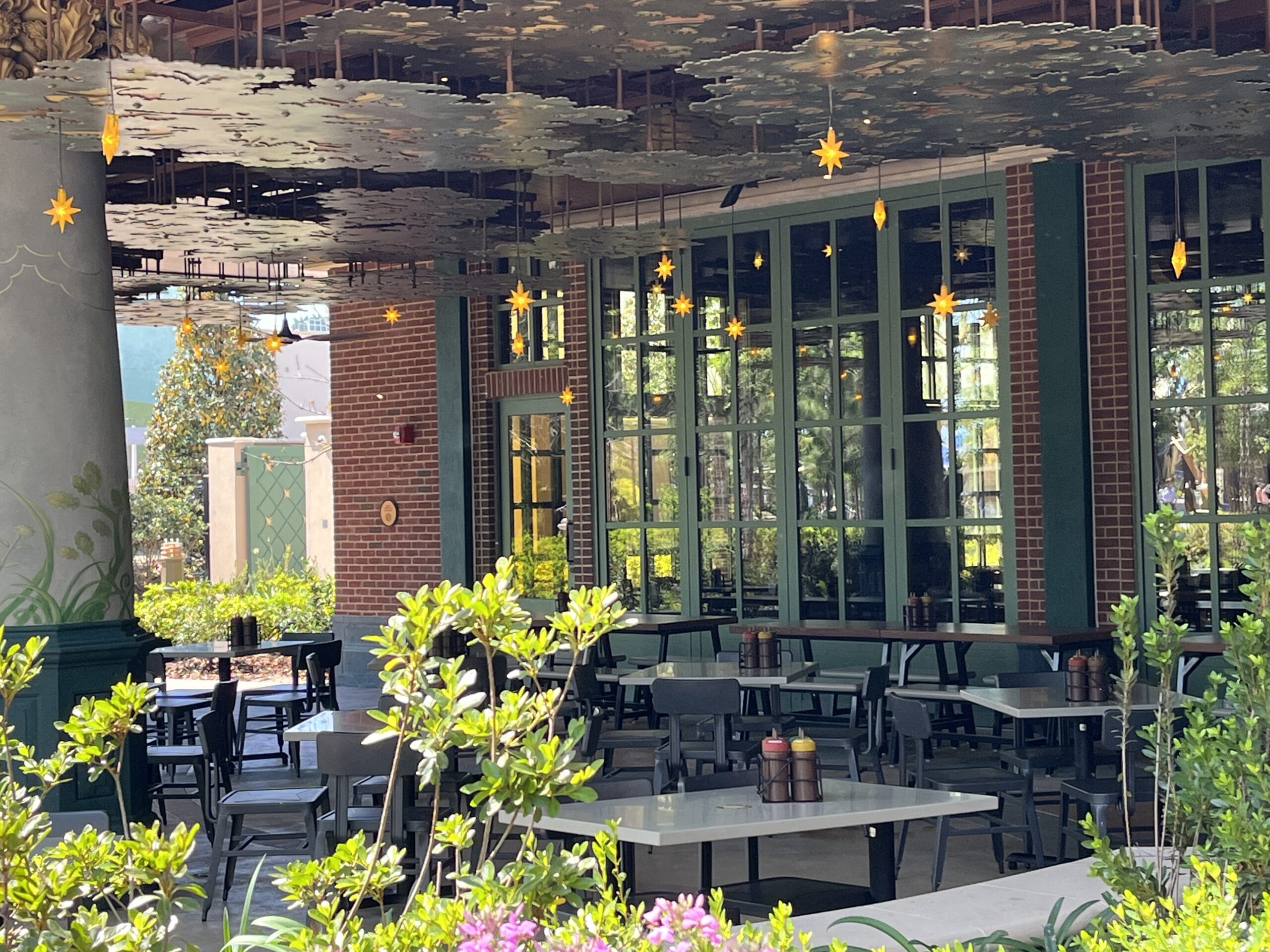 Charming outdoor patio at The Oak & Star Tavern, with empty tables, lush greenery, and glowing star lights—Disney parks ambiance.