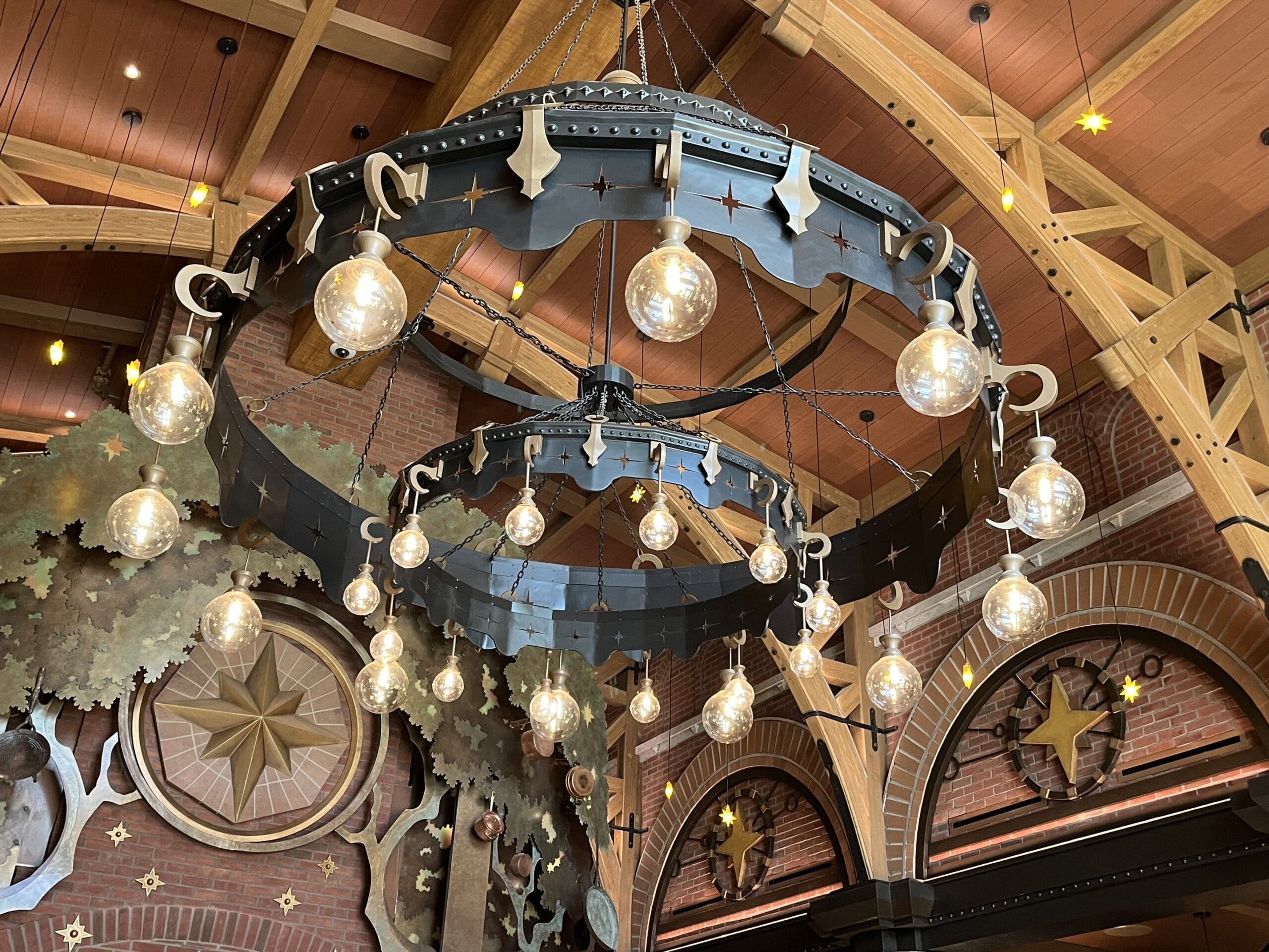 Large circular chandelier at The Oak & Star Tavern, under a wooden ceiling with star decor, like magical Disney touches, and brick arches.