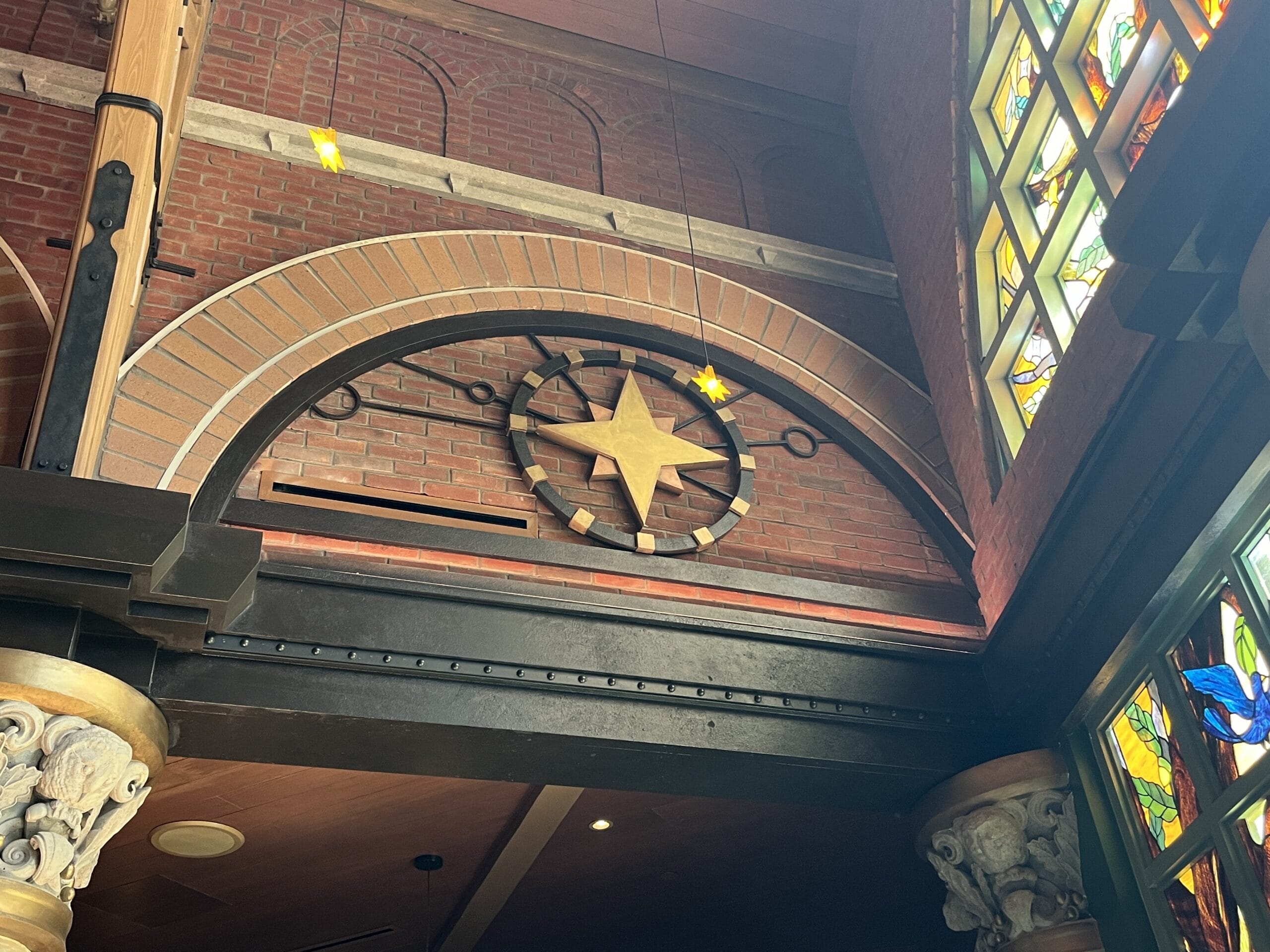 A wooden compass rose hangs near stained glass at The Oak & Star Tavern, with ornate columns like those at Disney park entrances.
