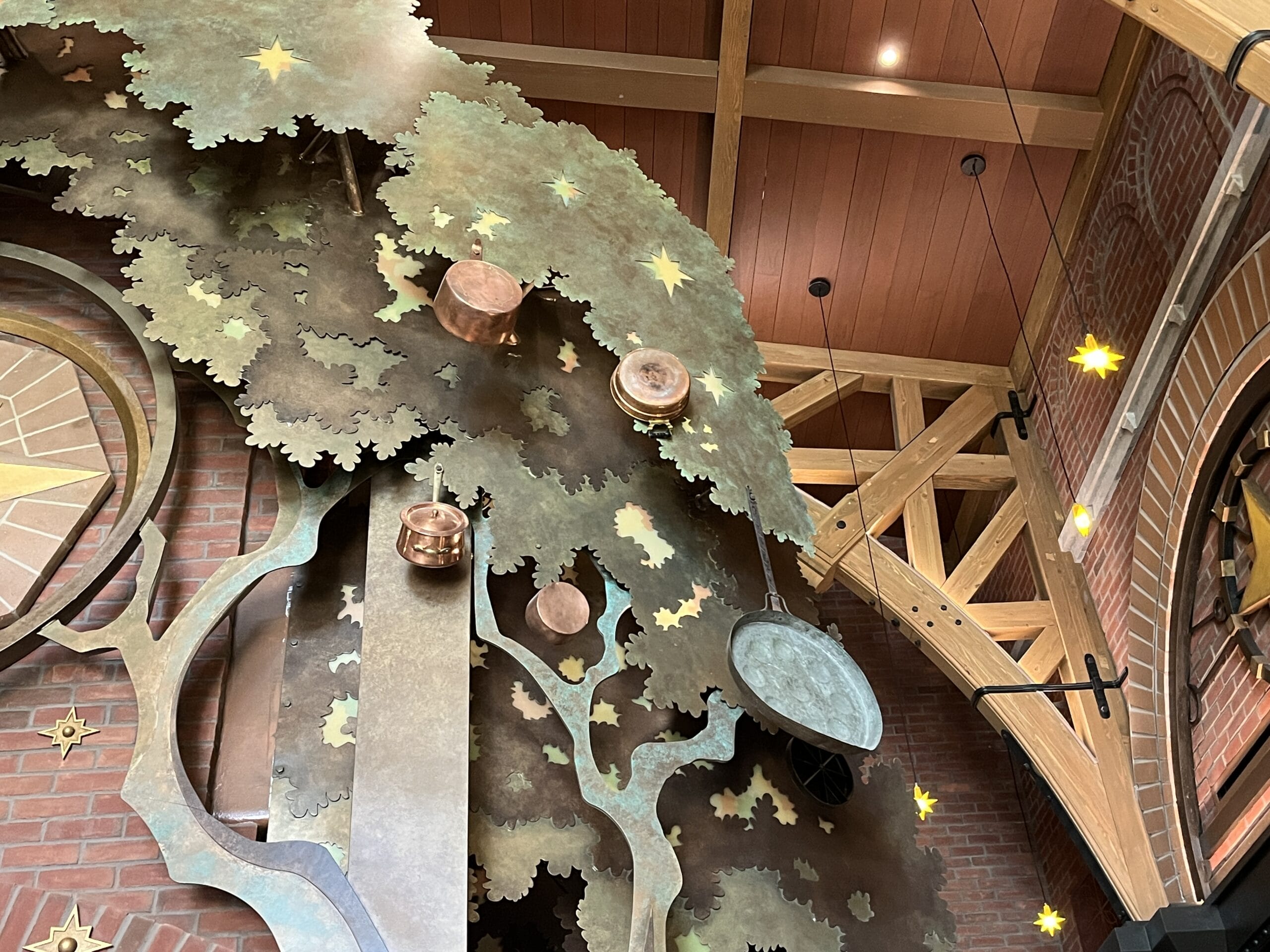 Copper pots and a pan hang from a metal tree at The Oak & Star Tavern, evoking Fantasyland charm with stars and wooden beams overhead.