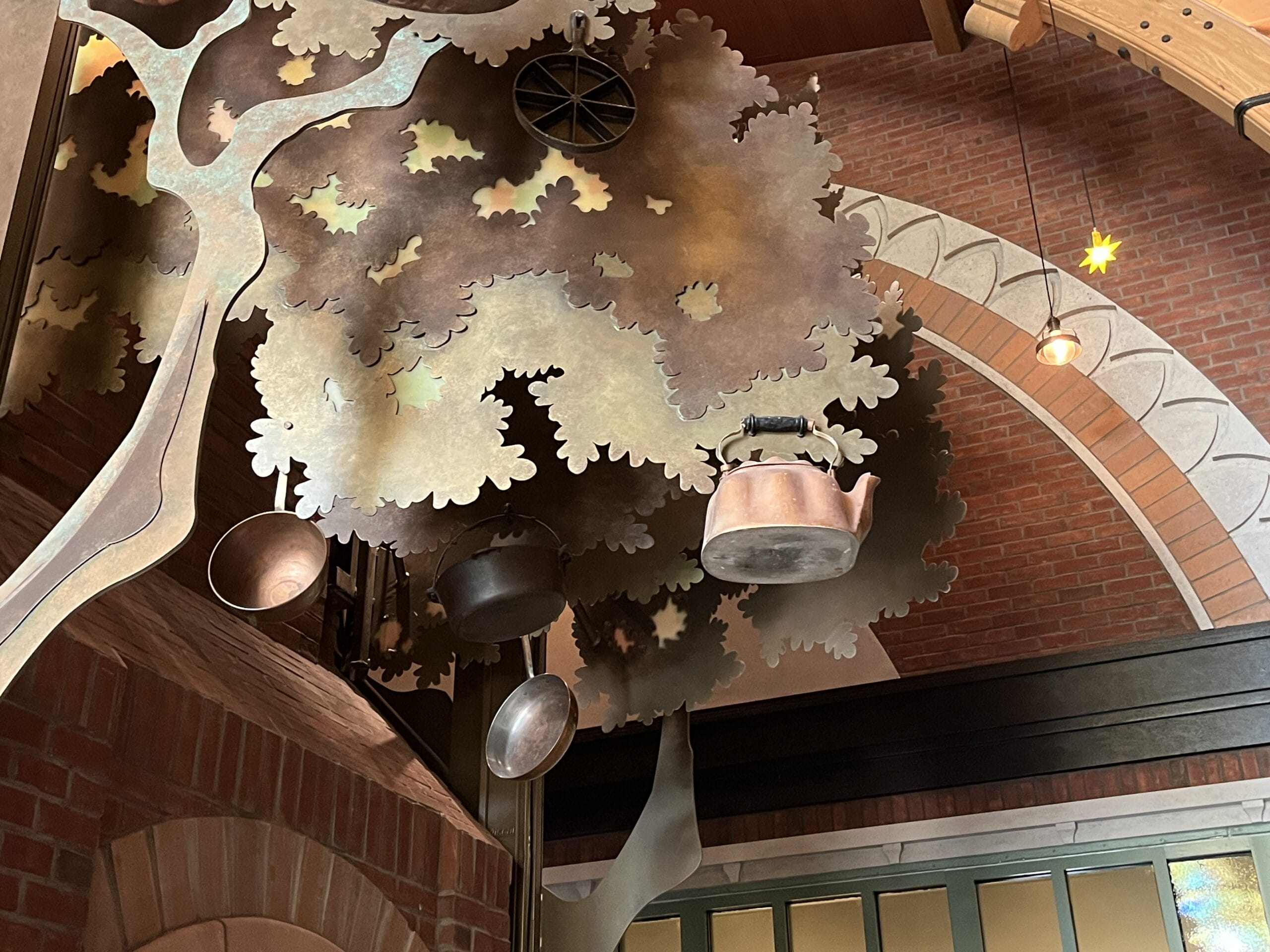 Metal tree sculpture with pots and a kettle at The Oak & Star Tavern, with brick wall and arched ceiling, similar to cozy Disney park decor.