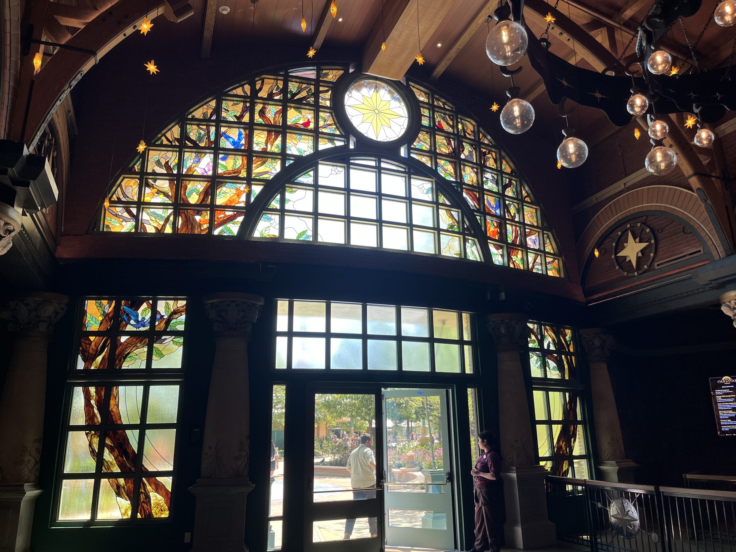 Stained glass archway with vibrant patterns and a star above The Oak & Star Tavern doors, people outside like Disney crowds.
