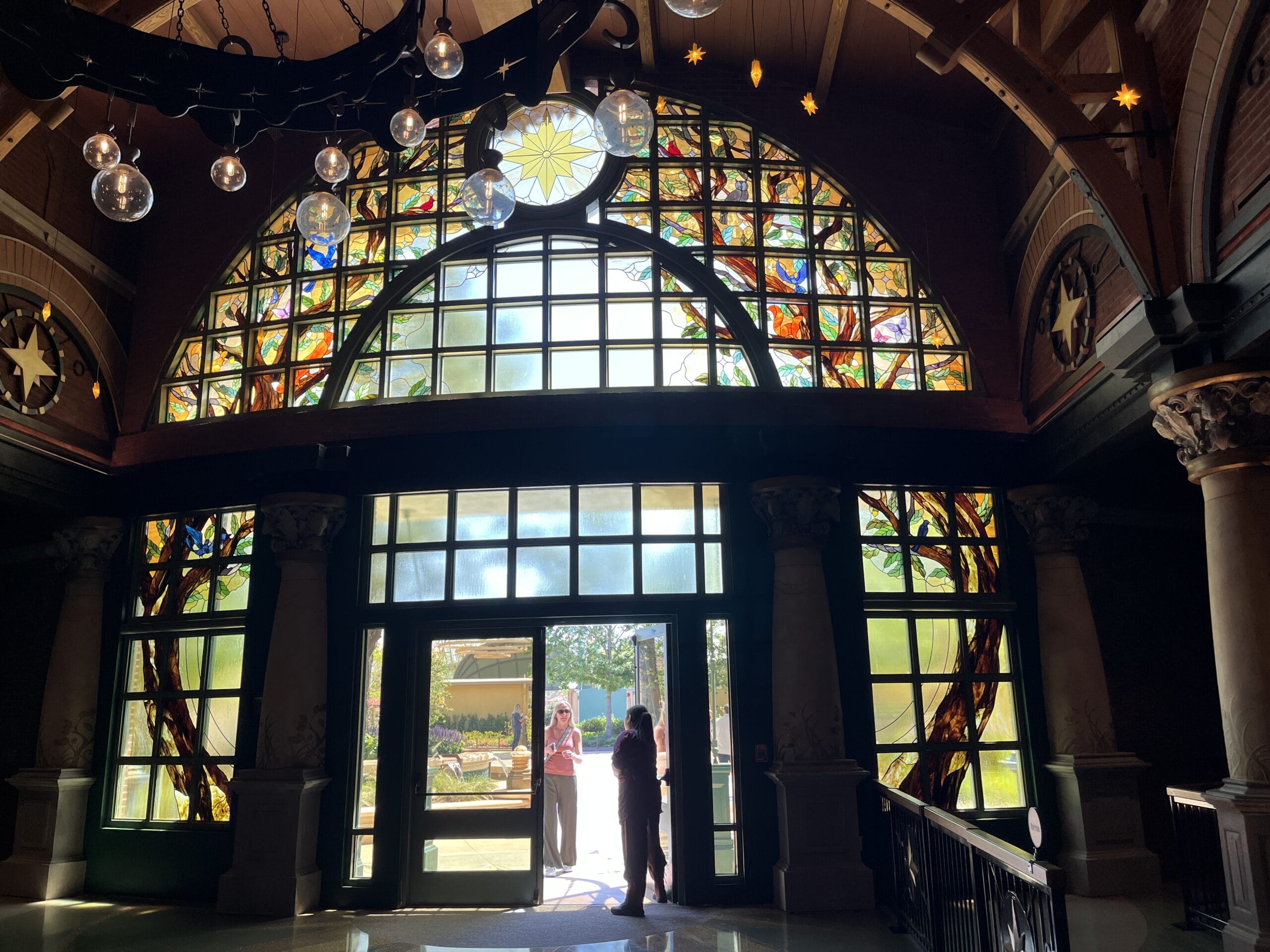 Two people stand at glass doors under The Oak & Star Tavern’s stained glass window, reminiscent of whimsical Disney park details.