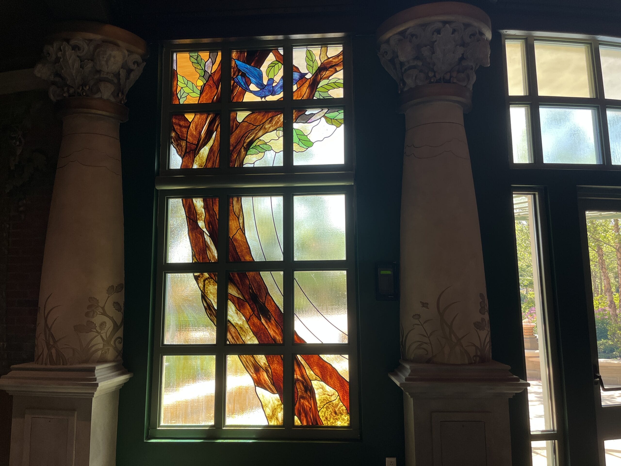 Stained glass window with a tree and blue bird at The Oak & Star Tavern, ornate columns like those in Disney’s Fantasyland castles.