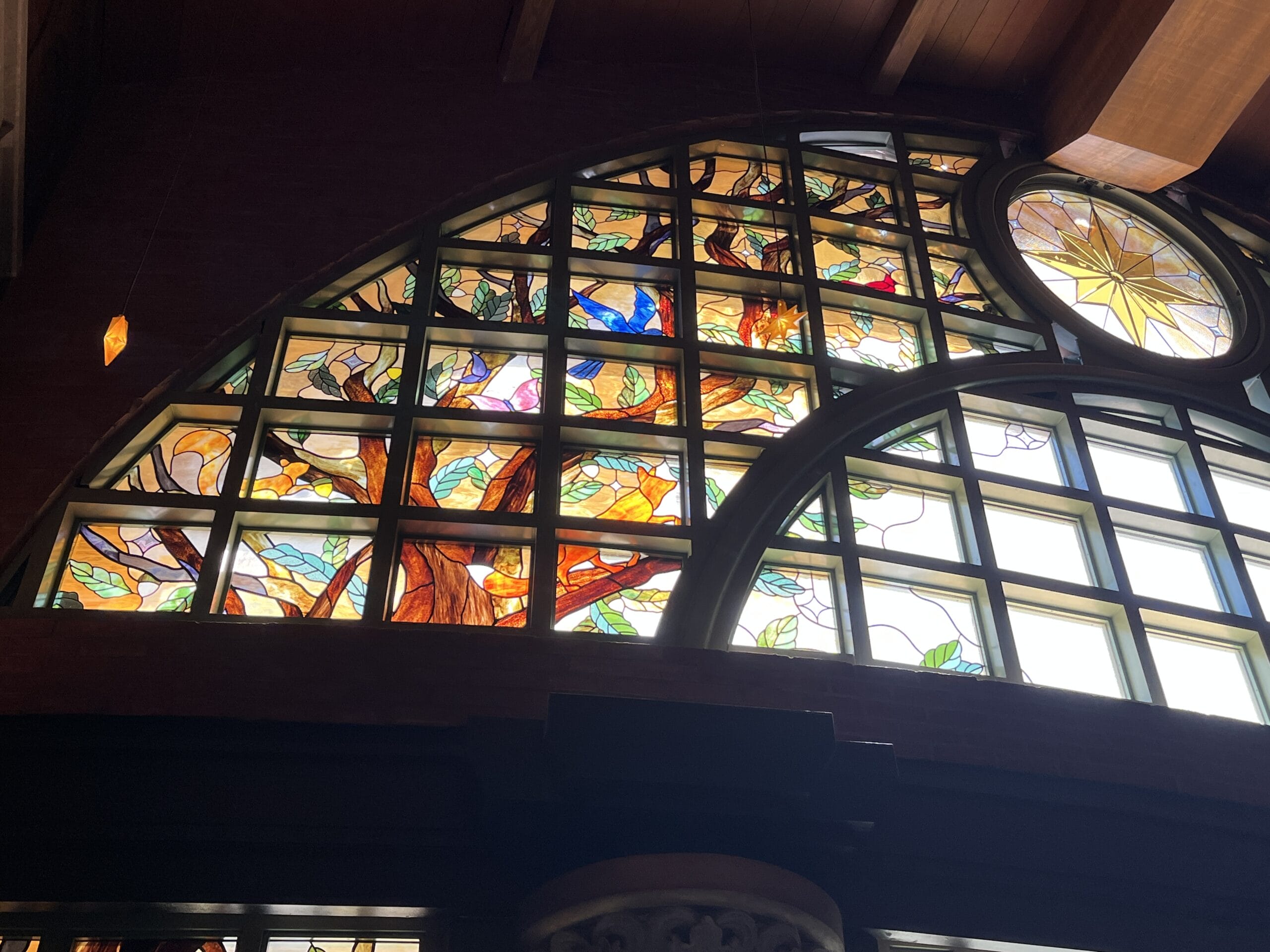 Stained glass window at The Oak & Star Tavern, its colorful tree glowing in sunlight—similar to Disney park window art styles.
