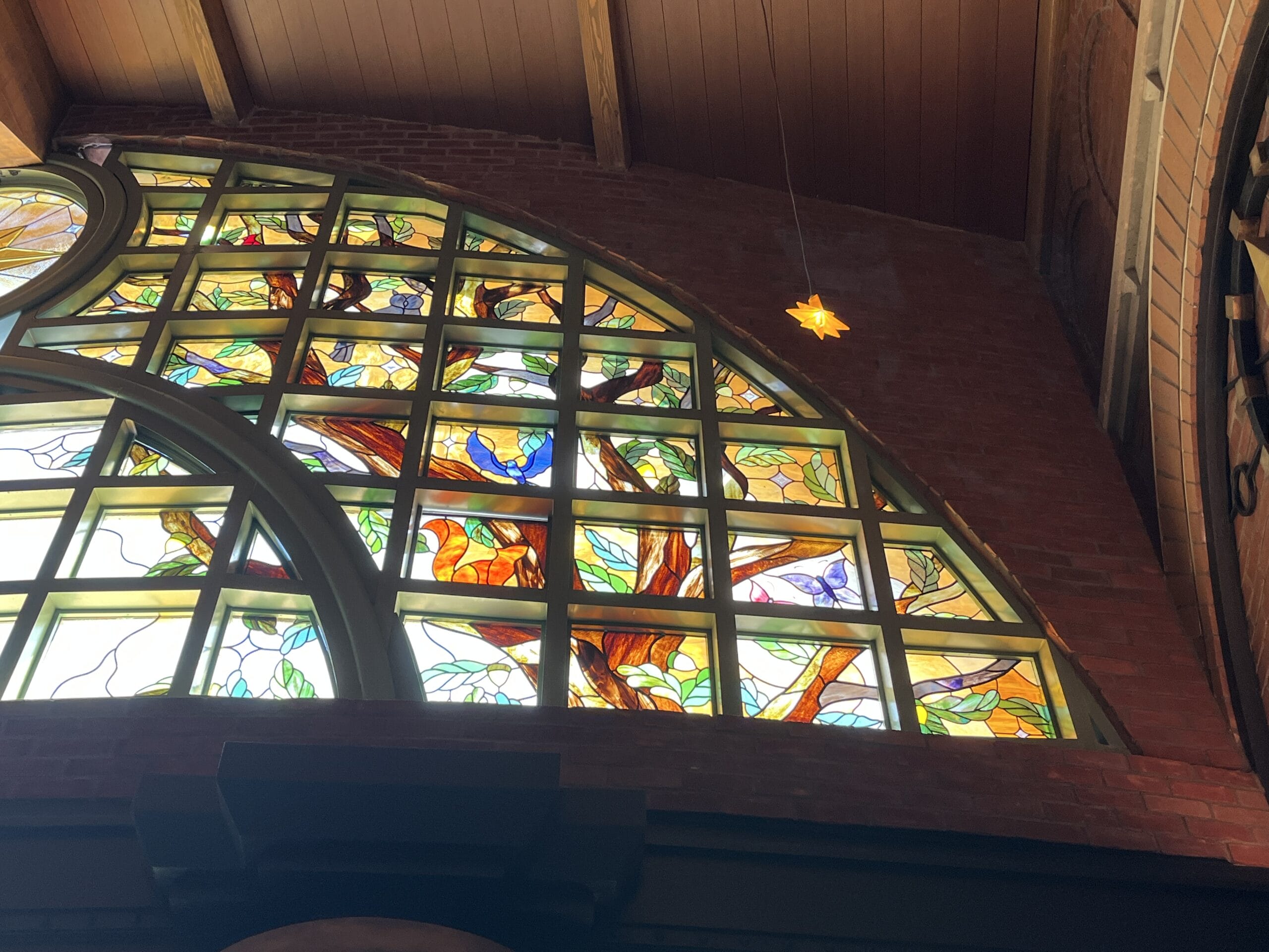 Stained glass window with colorful birds at The Oak & Star Tavern, set in a brick wall under a glowing star light—no Disney castle.