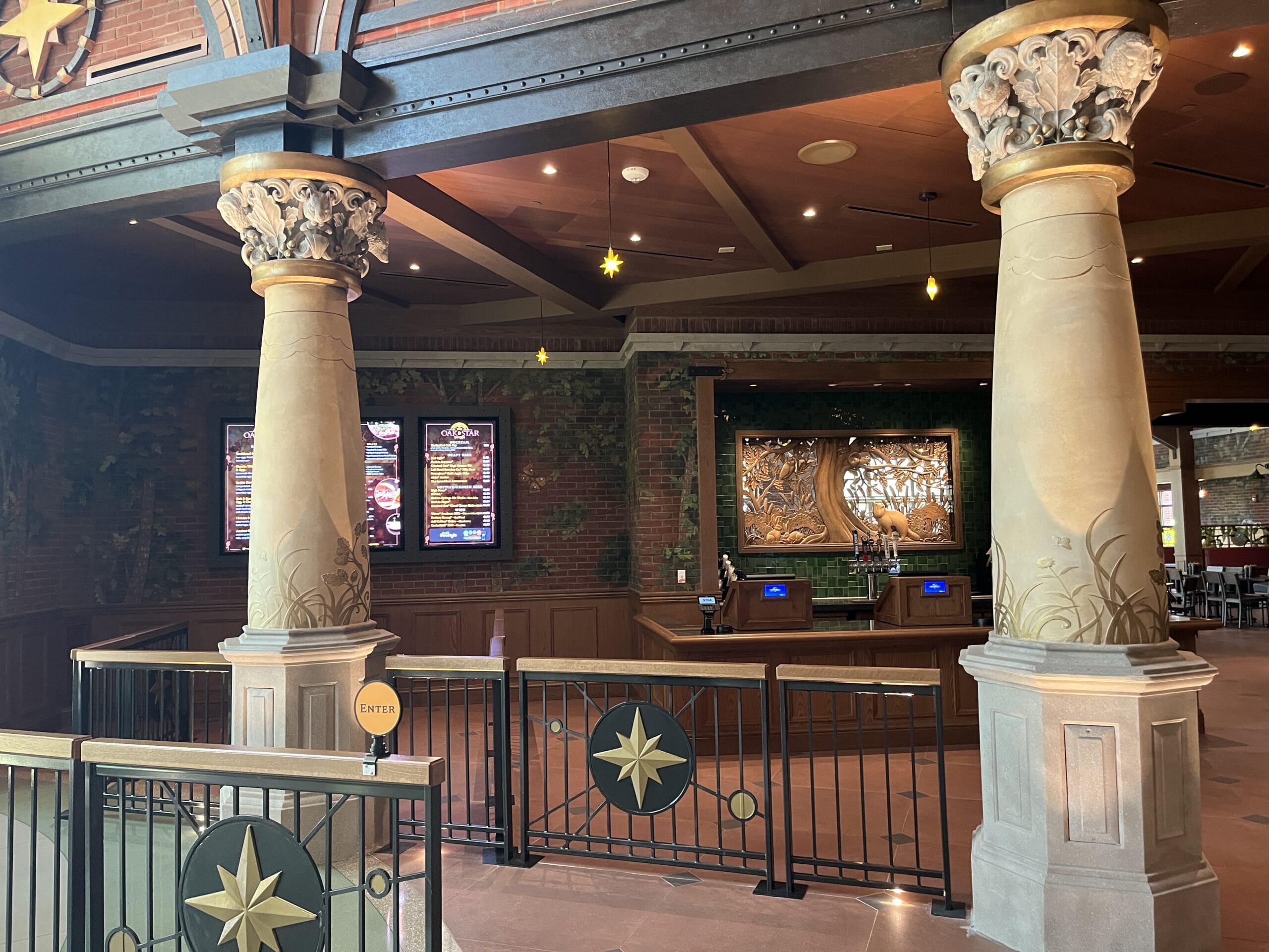 The Oak & Star Tavern entrance displays ornate columns, starry railings, digital menus, and a carved counter, evoking Disney park elegance.