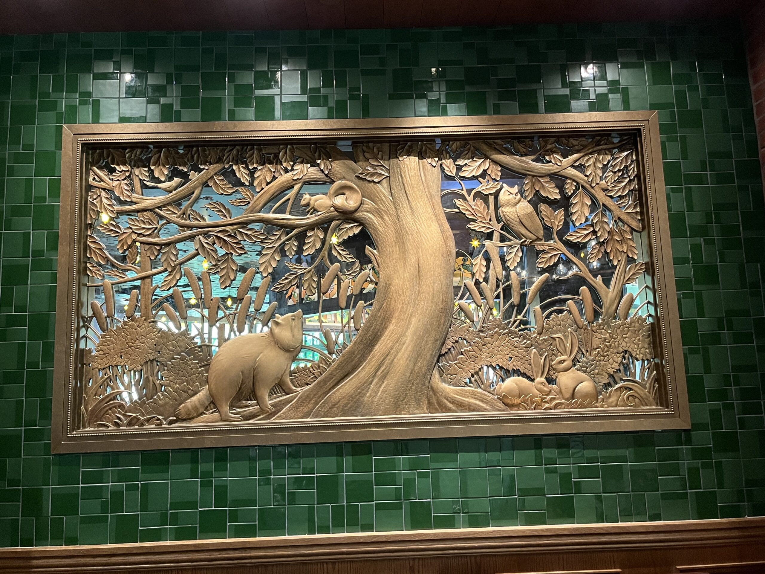 Wooden wall art of a tree with a bear, squirrel, and rabbits, reminiscent of Disney park rustic decor but without castle elements.