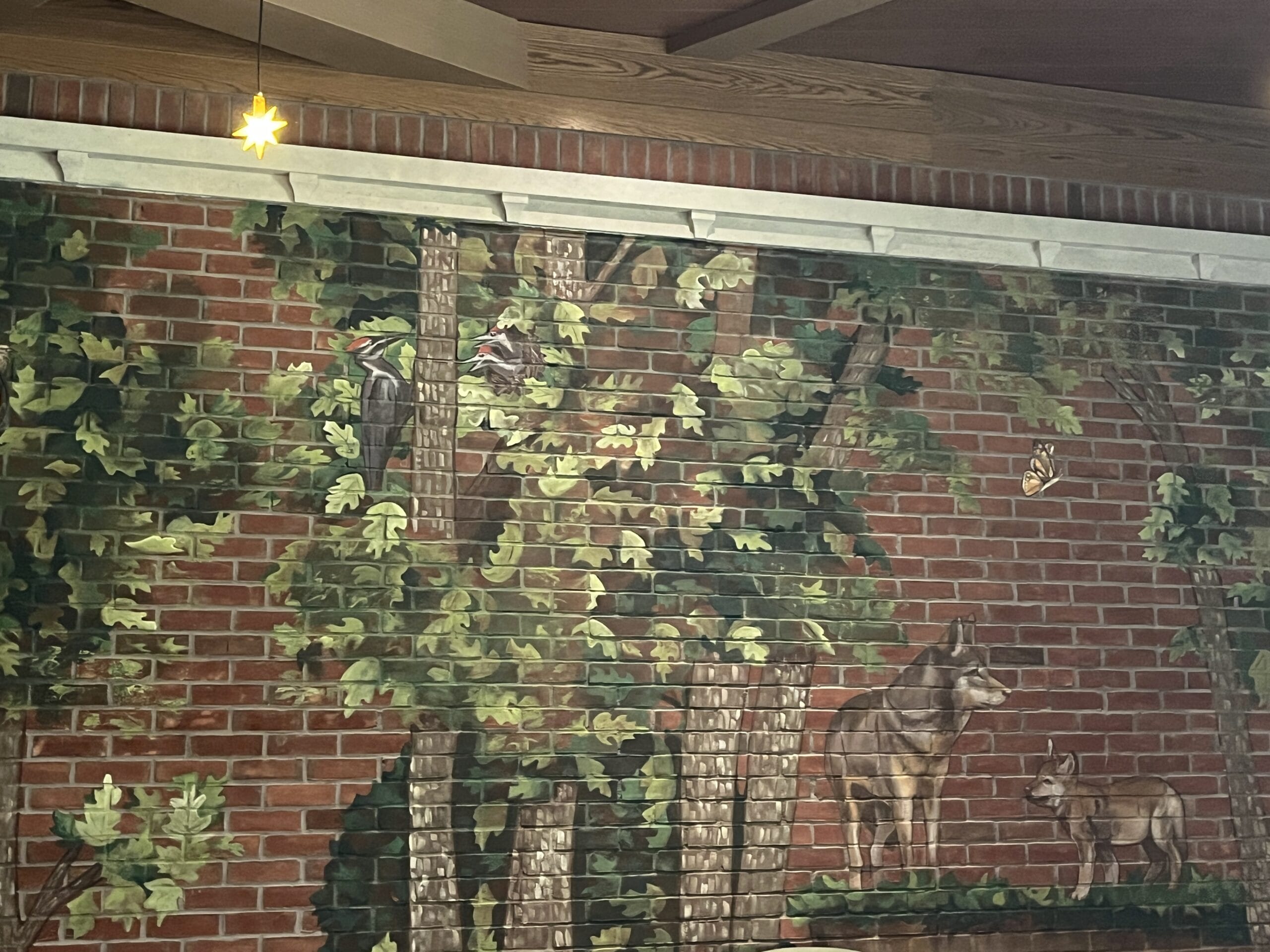 A mural at The Oak & Star Tavern shows trees, leaves, two wolves, a butterfly, and a light above—not a Disney castle scene.