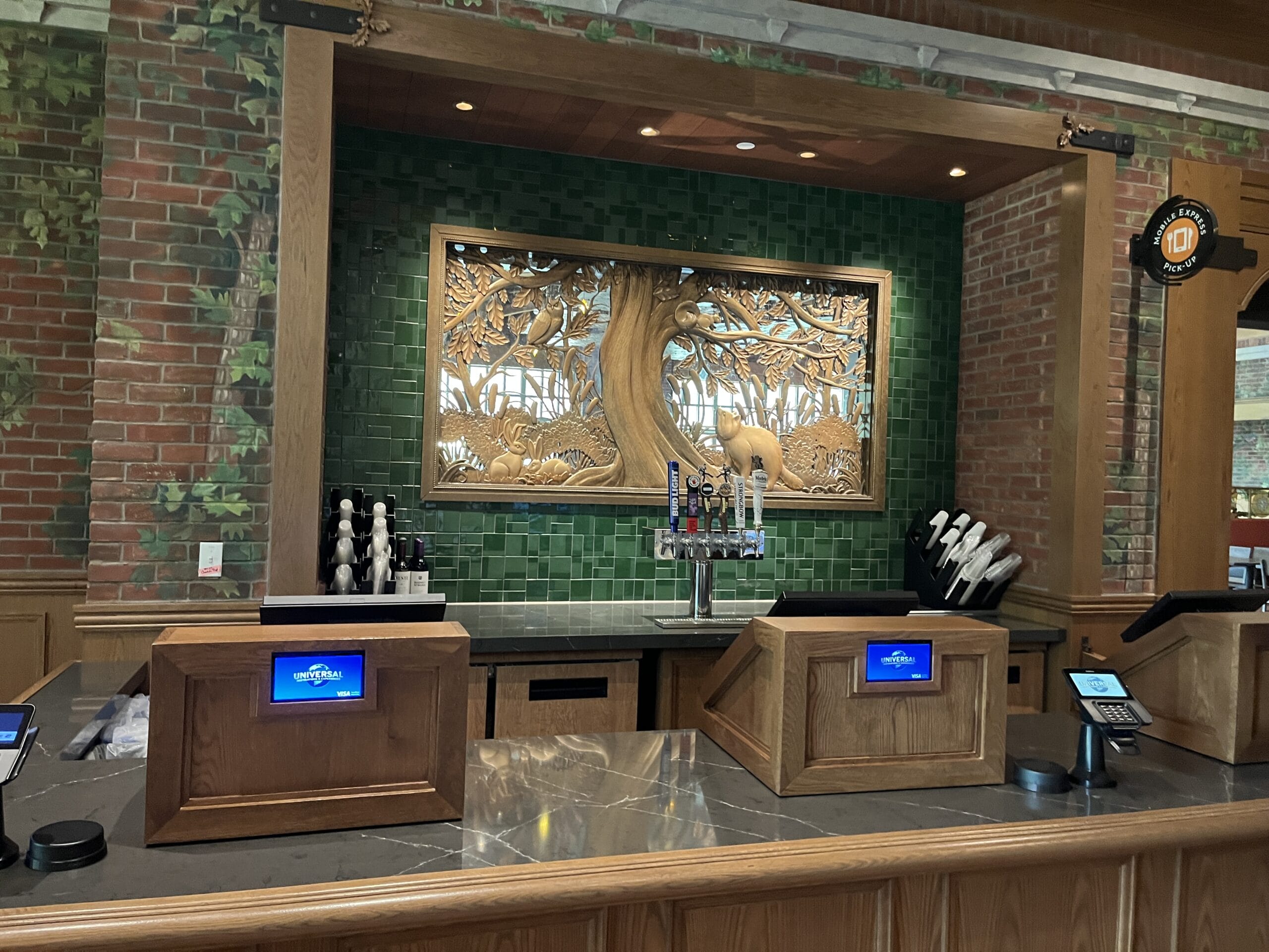 A counter with registers, beer taps, and a large tree mural at The Oak & Star Tavern, reminiscent of Animal Kingdom theming.