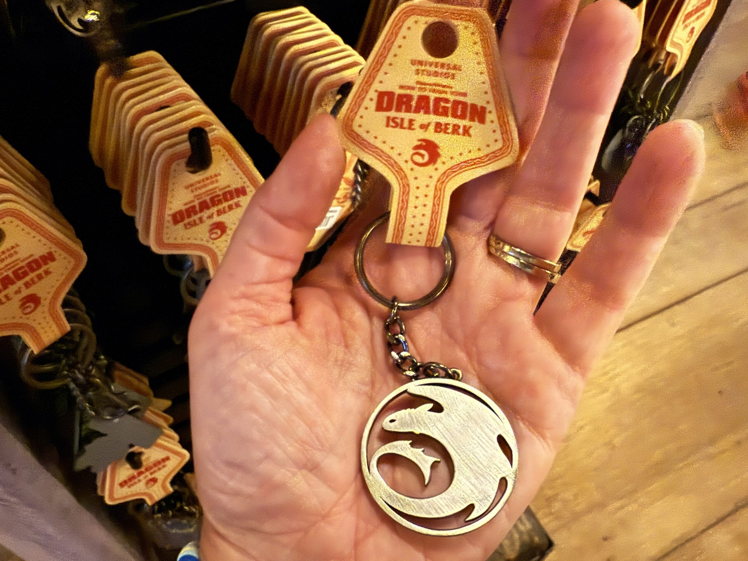 A hand holds a "Dragon: Isle of Berk" keychain from Universal Studios, inspired by Viking Traders.