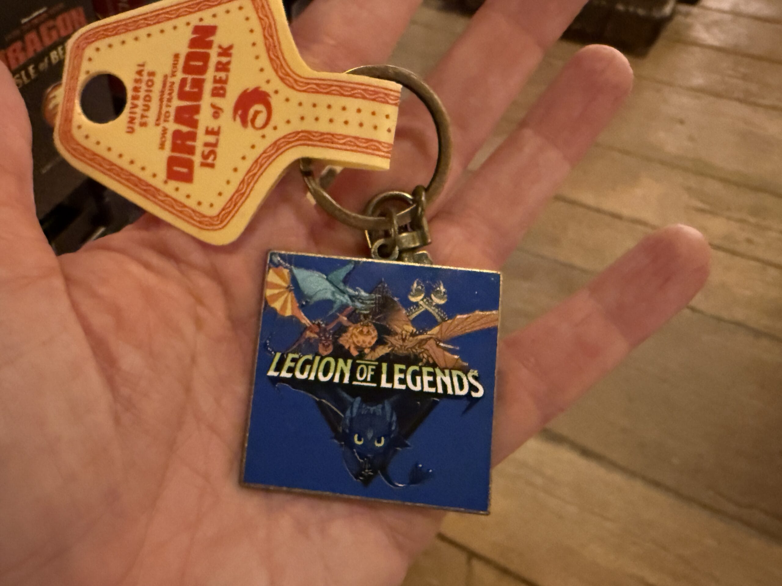 A hand holds a "Legion of Legends" keychain with a dragon design from Viking Traders and an Isle of Berk tag.