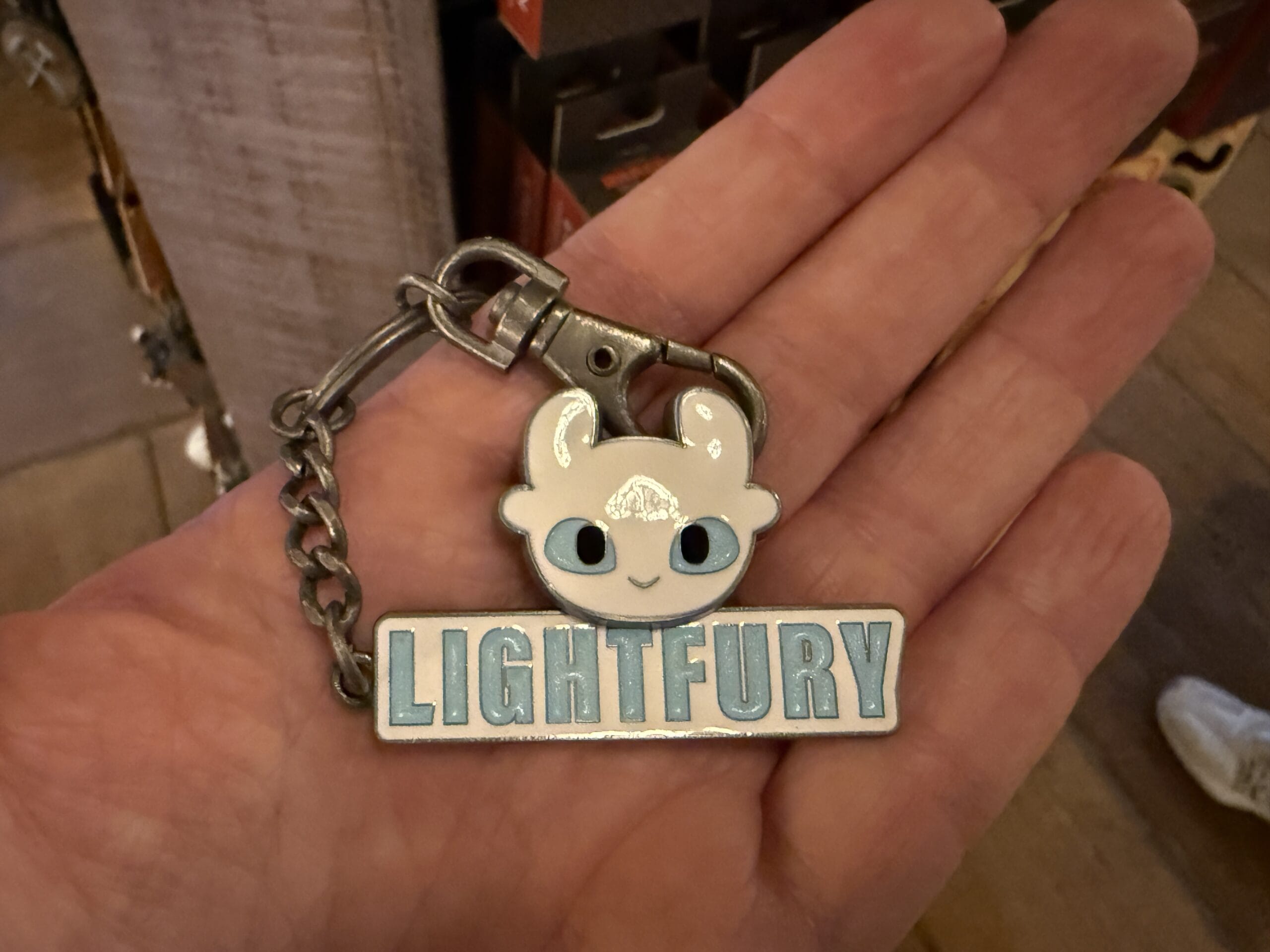 A hand holds a Viking Traders keychain with a cute dragon face and the word "LIGHTFURY" in blue letters.