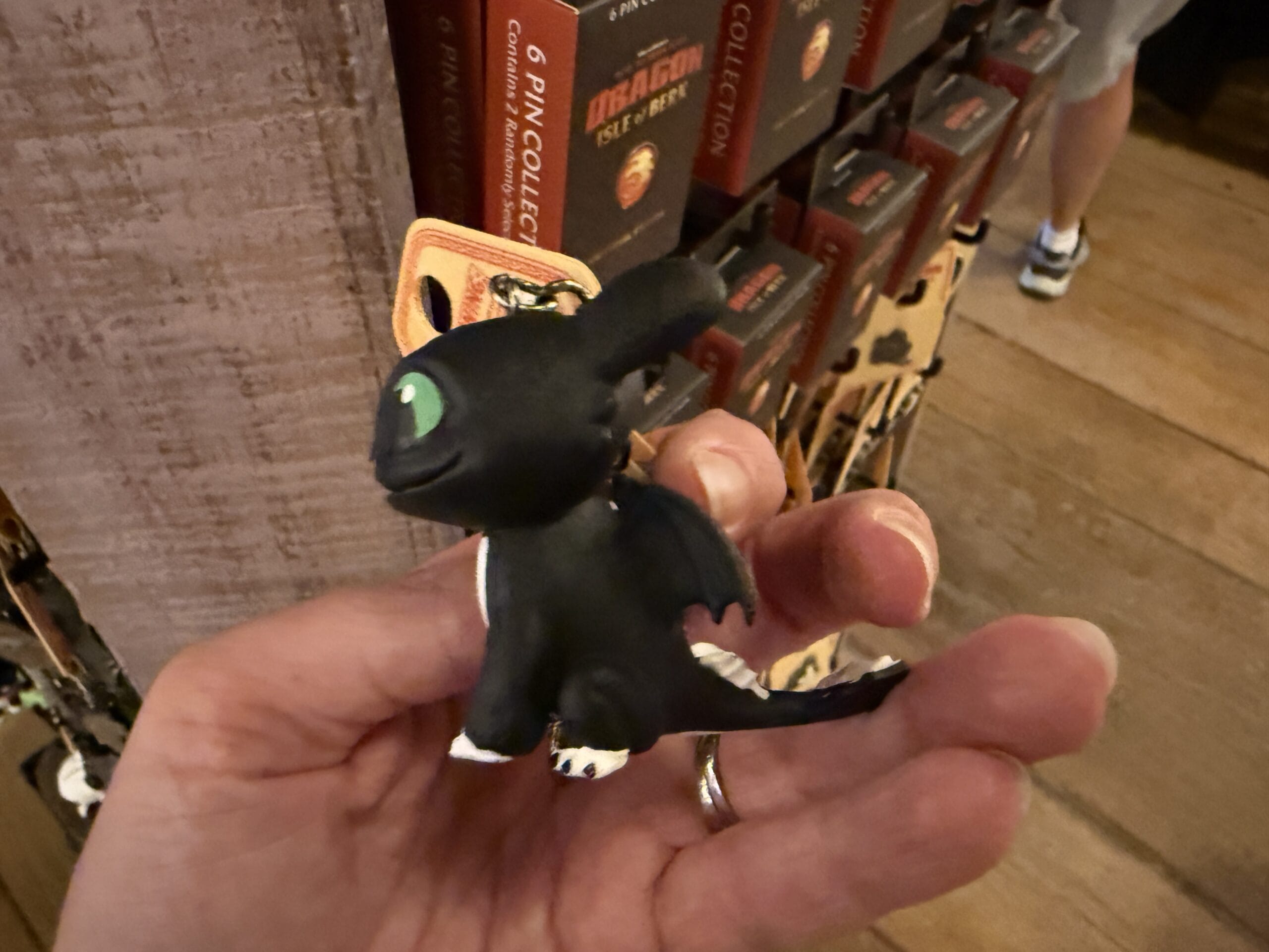 A hand holds a small Toothless plush keychain in a store, perfect for fans of Viking Traders and "How to Train Your Dragon.