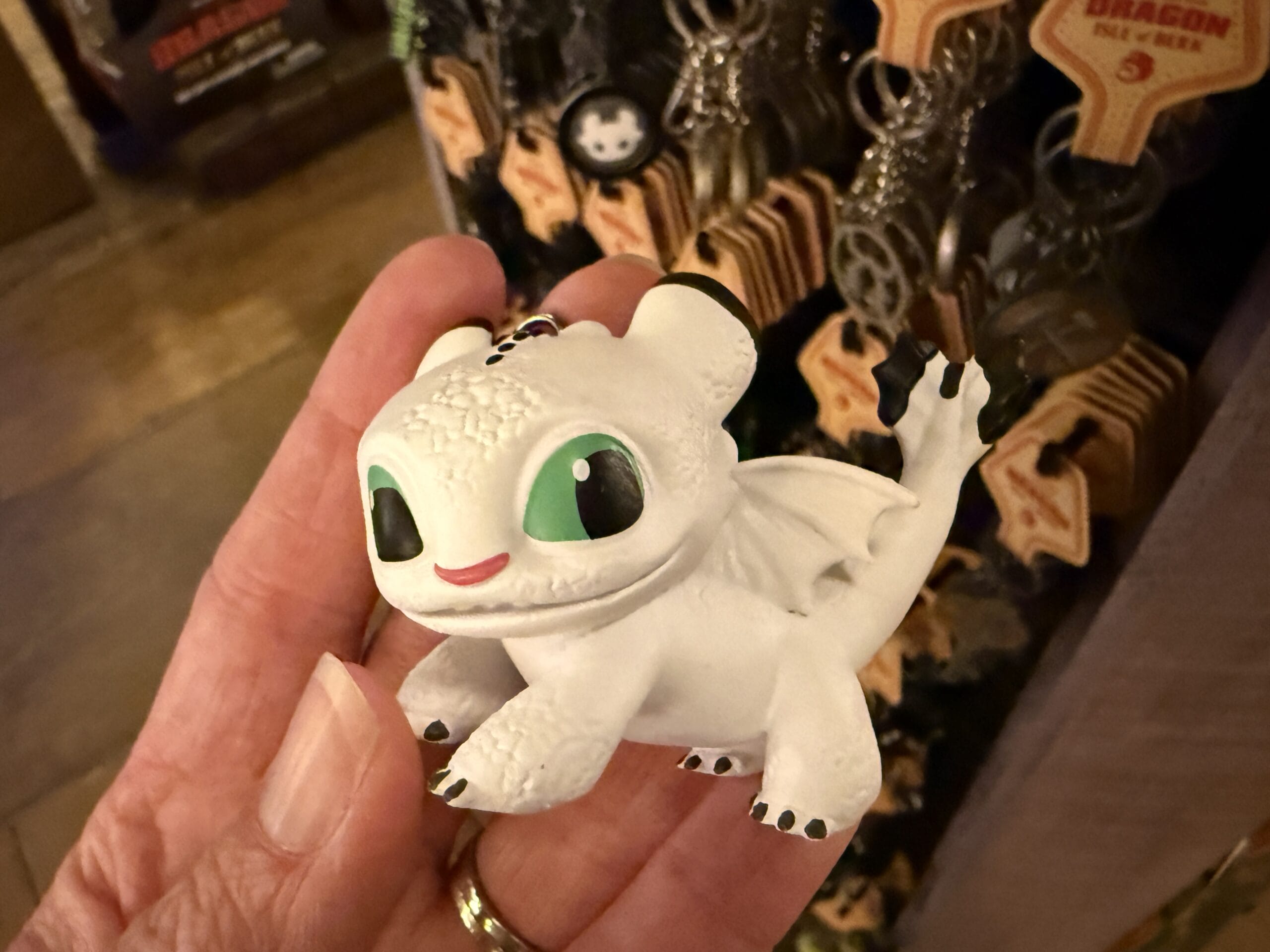 A hand holds a Viking Traders small white dragon figurine keychain with green eyes and a smiling face.