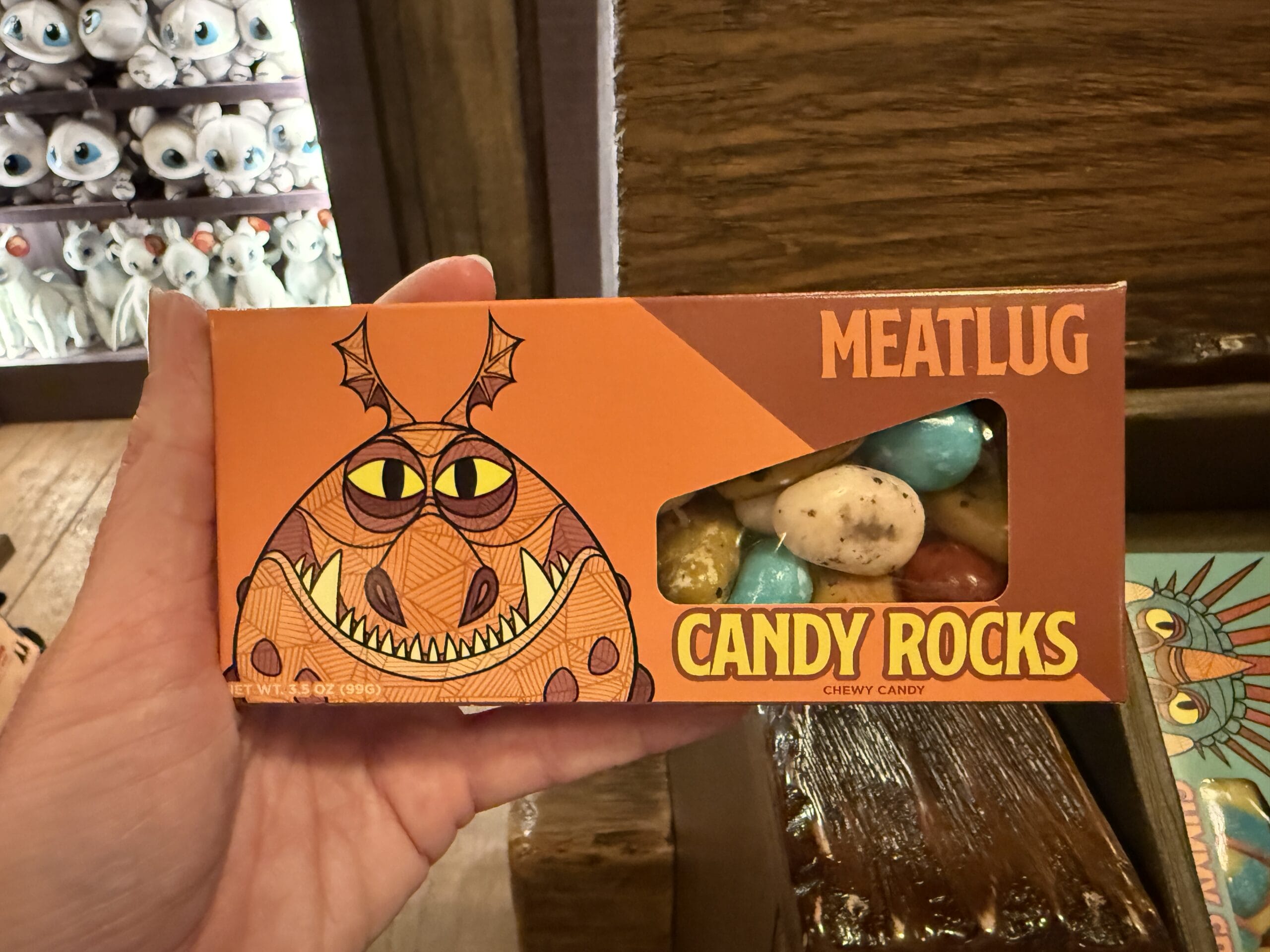 A hand holds a box of Meatlug Candy Rocks from Viking Traders, featuring cartoon dragon art and colorful candy windows.