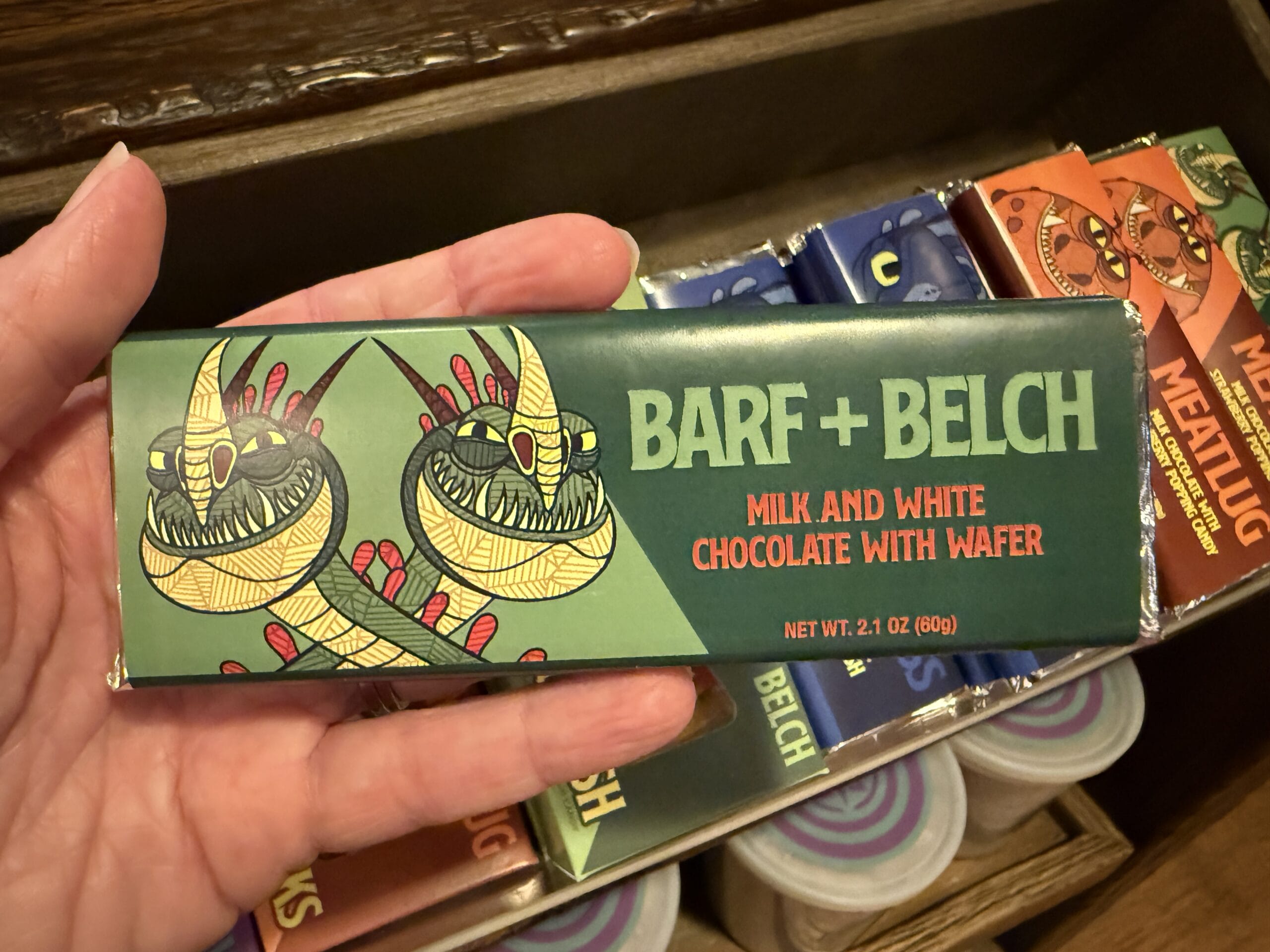 A hand holds a "BARF + BELCH" chocolate bar from Viking Traders, with cartoon dragons and bold text on the wrapper.