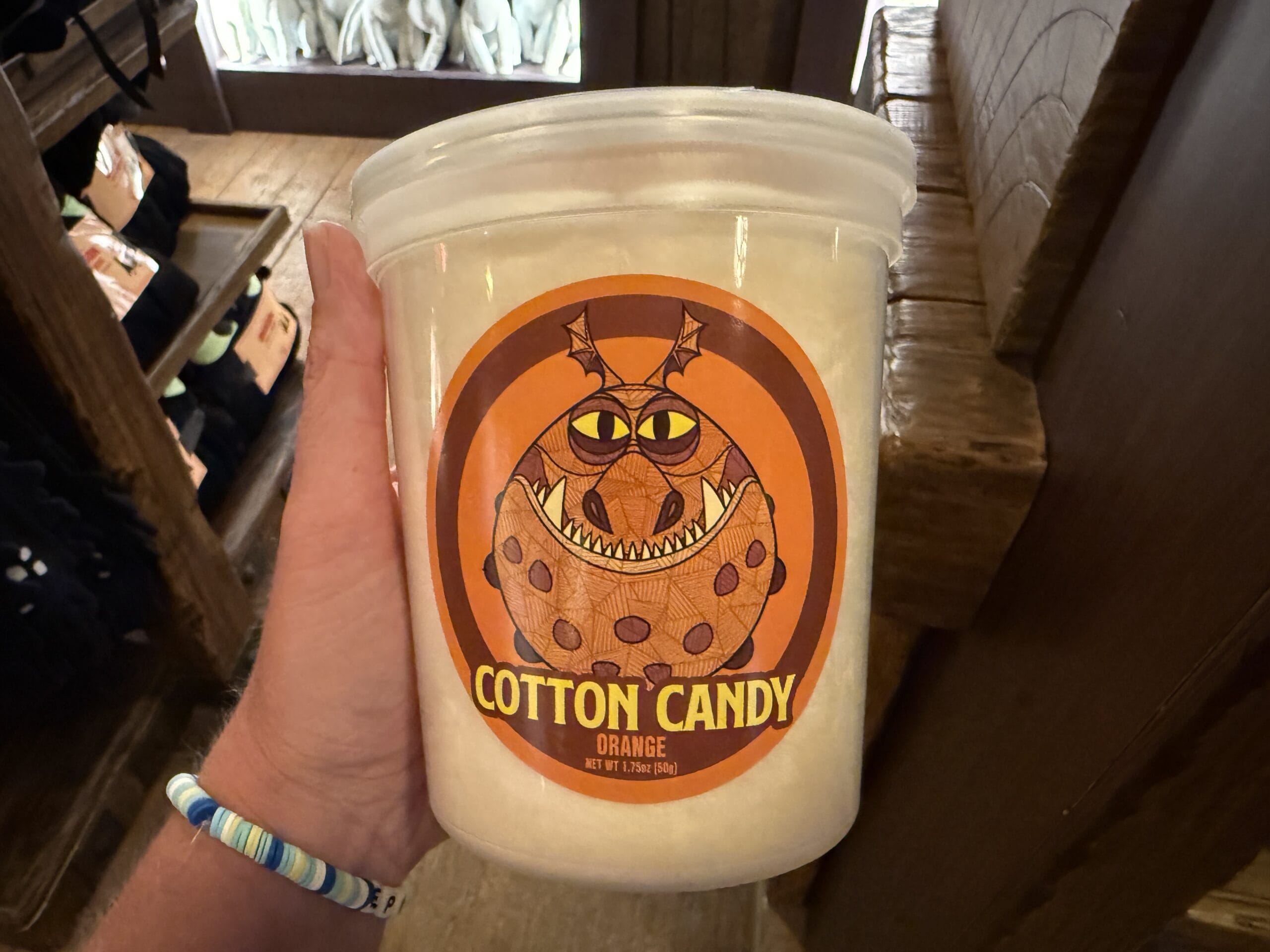 A hand holds a tub of orange cotton candy from Viking Traders, featuring a cartoon monster on the label.