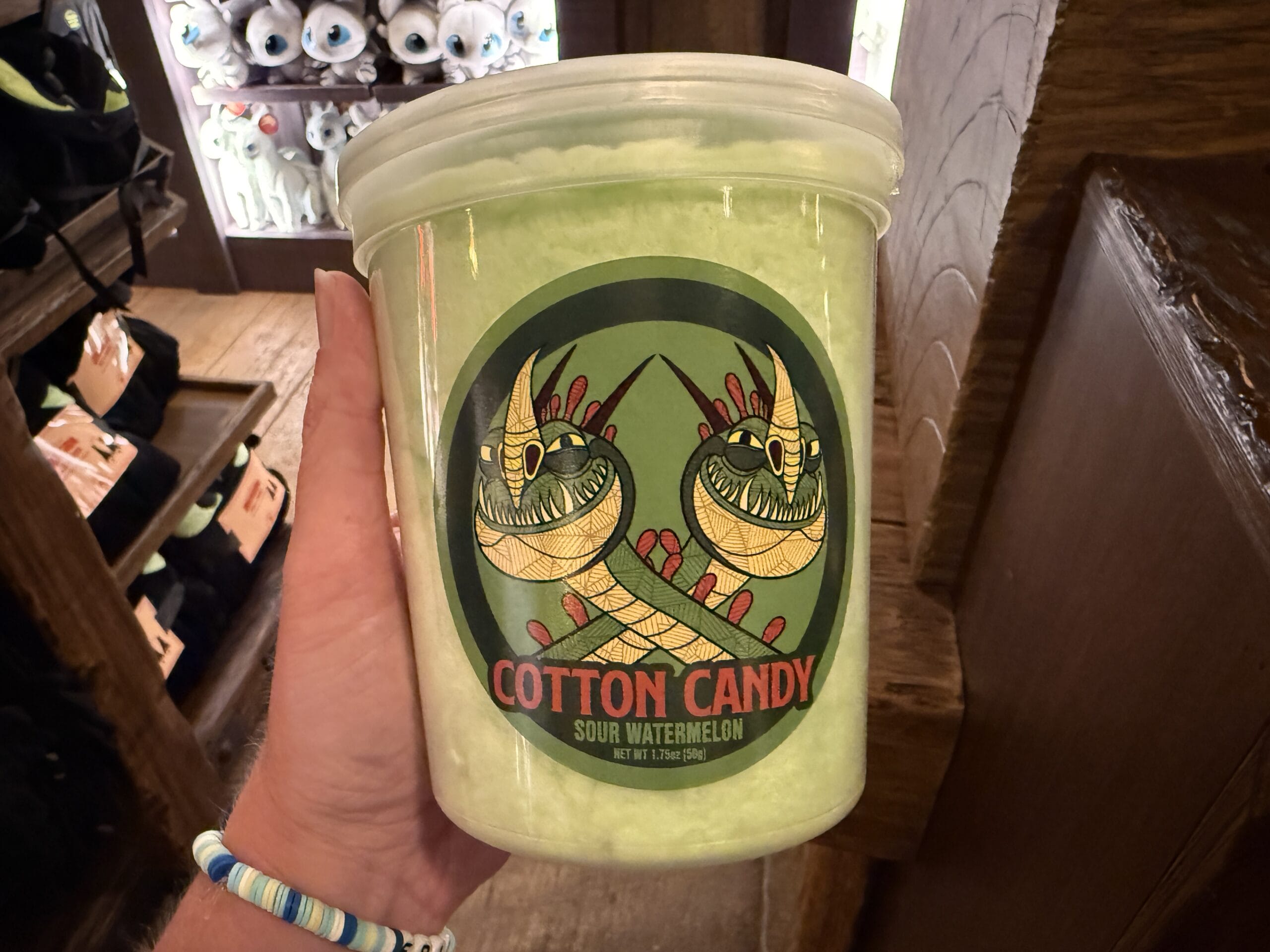 A hand holds a tub of Viking Traders sour watermelon cotton candy with a green dragon design on the label.