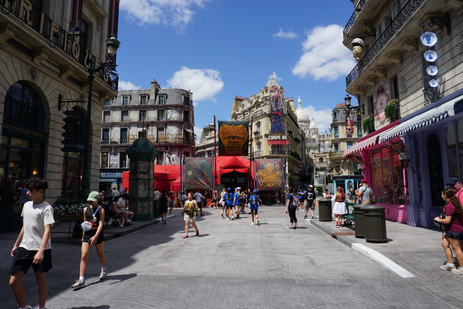 People stroll a lively, decorated street in the Wizarding World of Harry Potter, lined with colorful banners and ornate shops.