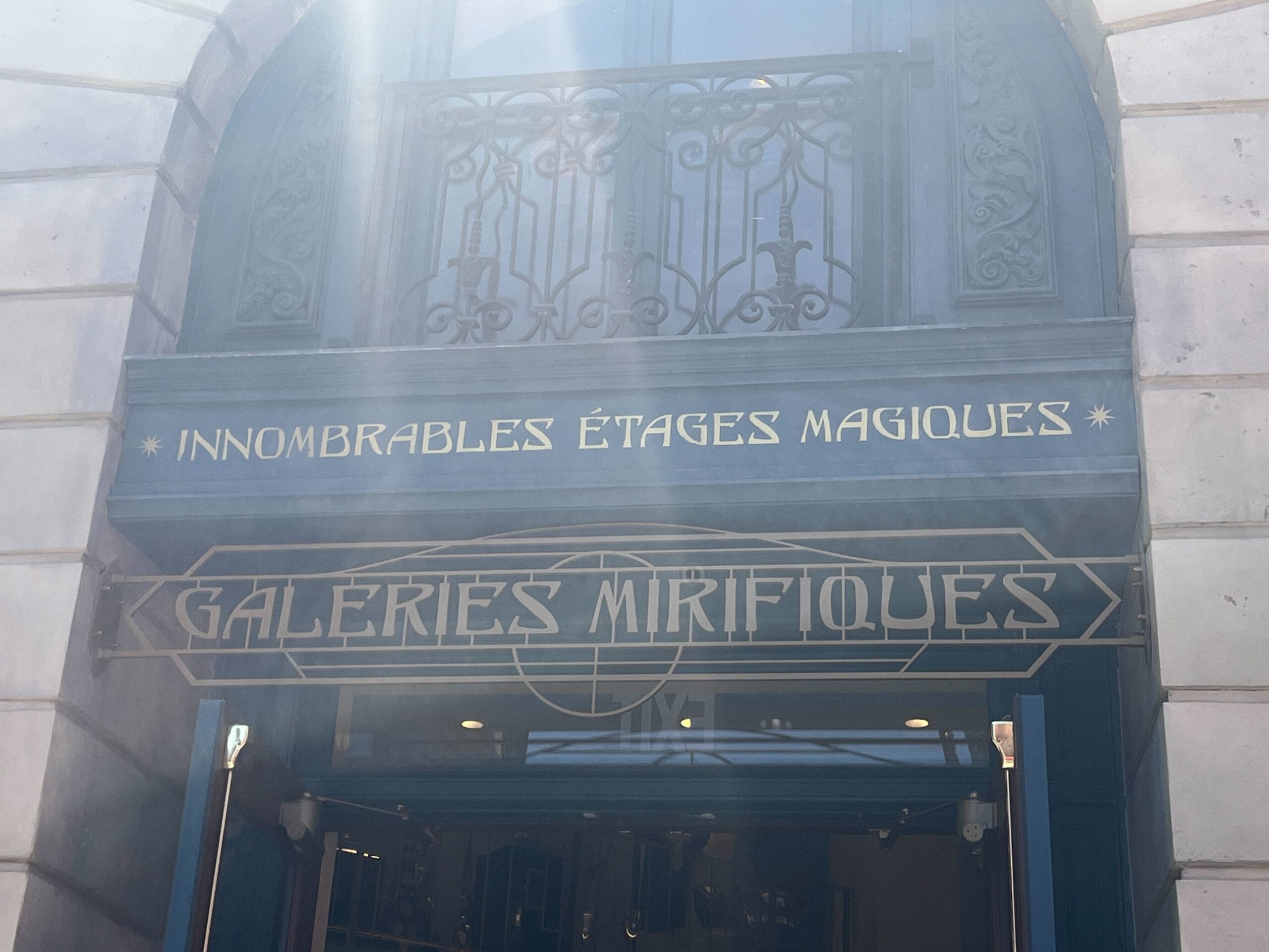 A blue awning reads "INNOMBRABLES ÉTAGES MAGIQUES" and "Les Galeries Mirifiques" outside a building entrance.