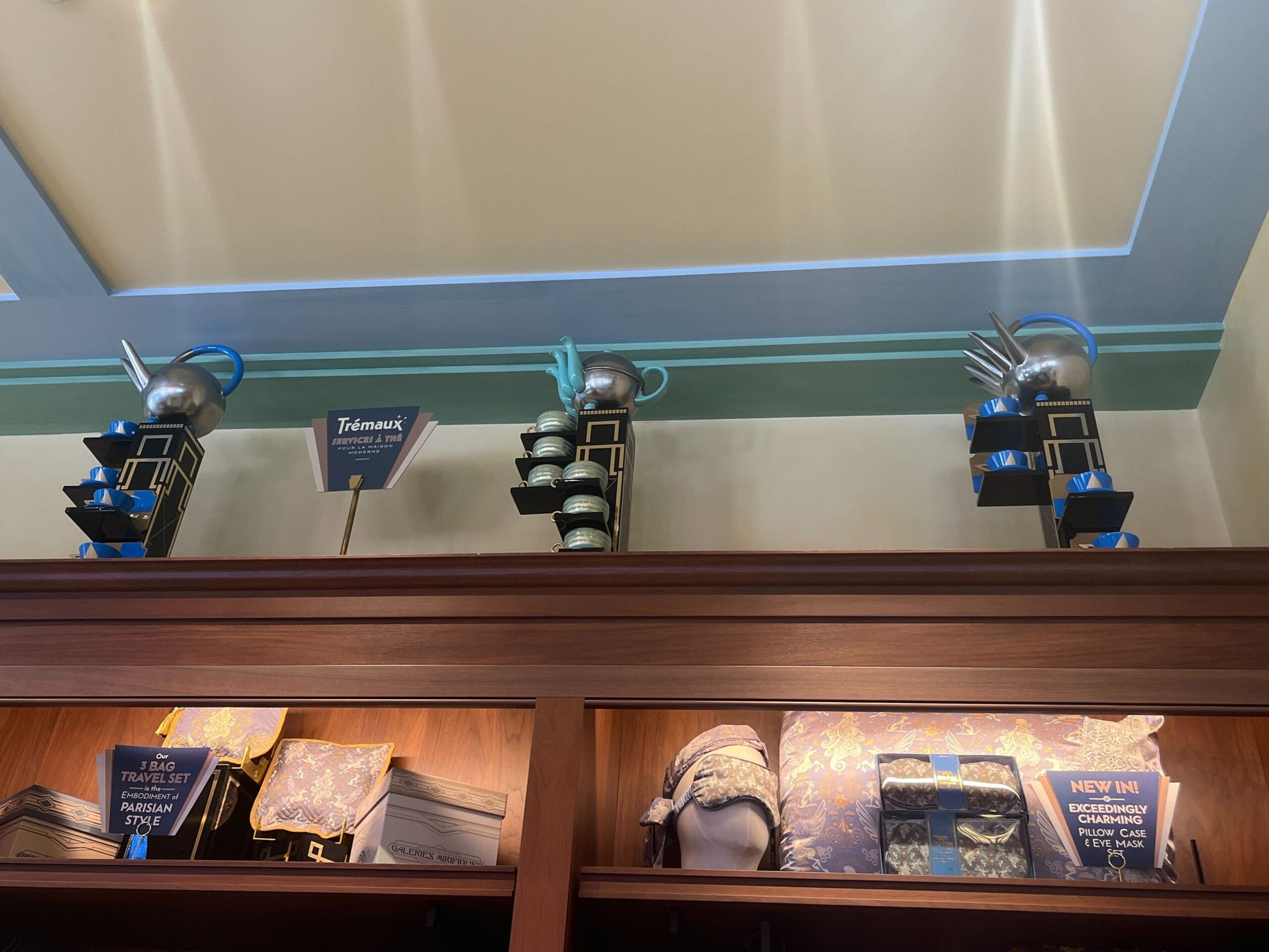 Shelves at Les Galeries Mirifiques display teapots, mugs, bags, and scarves under a "Teawares" sign.