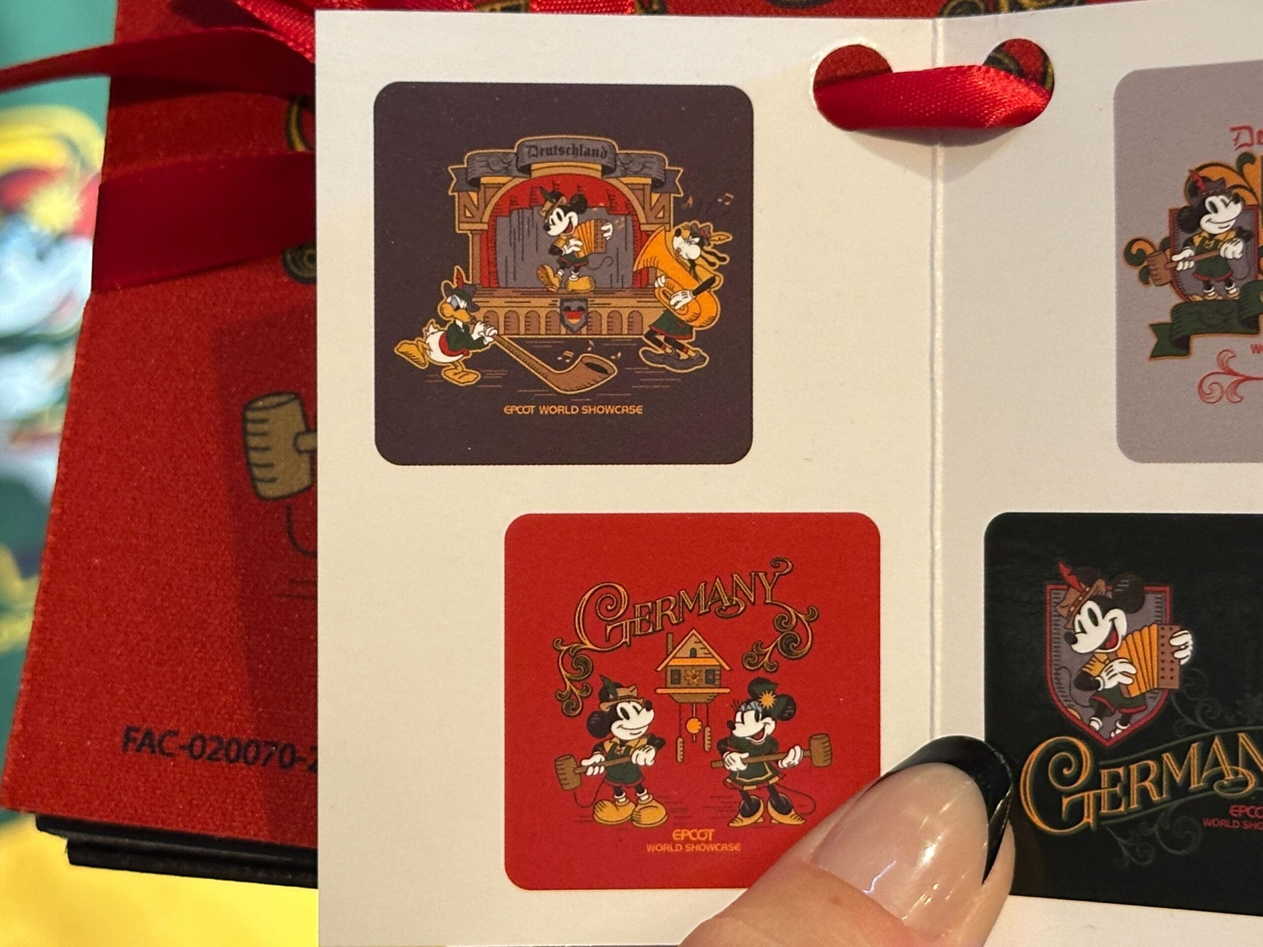A hand holds a card with Germany-themed Mickey Mouse stickers, a fun merchandise find at EPCOT's Germany Pavilion.