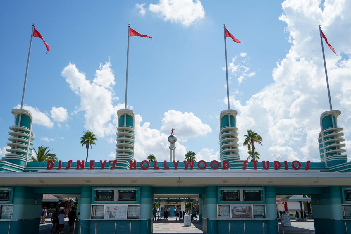 Hollywood Studios Entrance with art deco design, red flags, palm trees, and a blue sky—What to Know Before You Go.