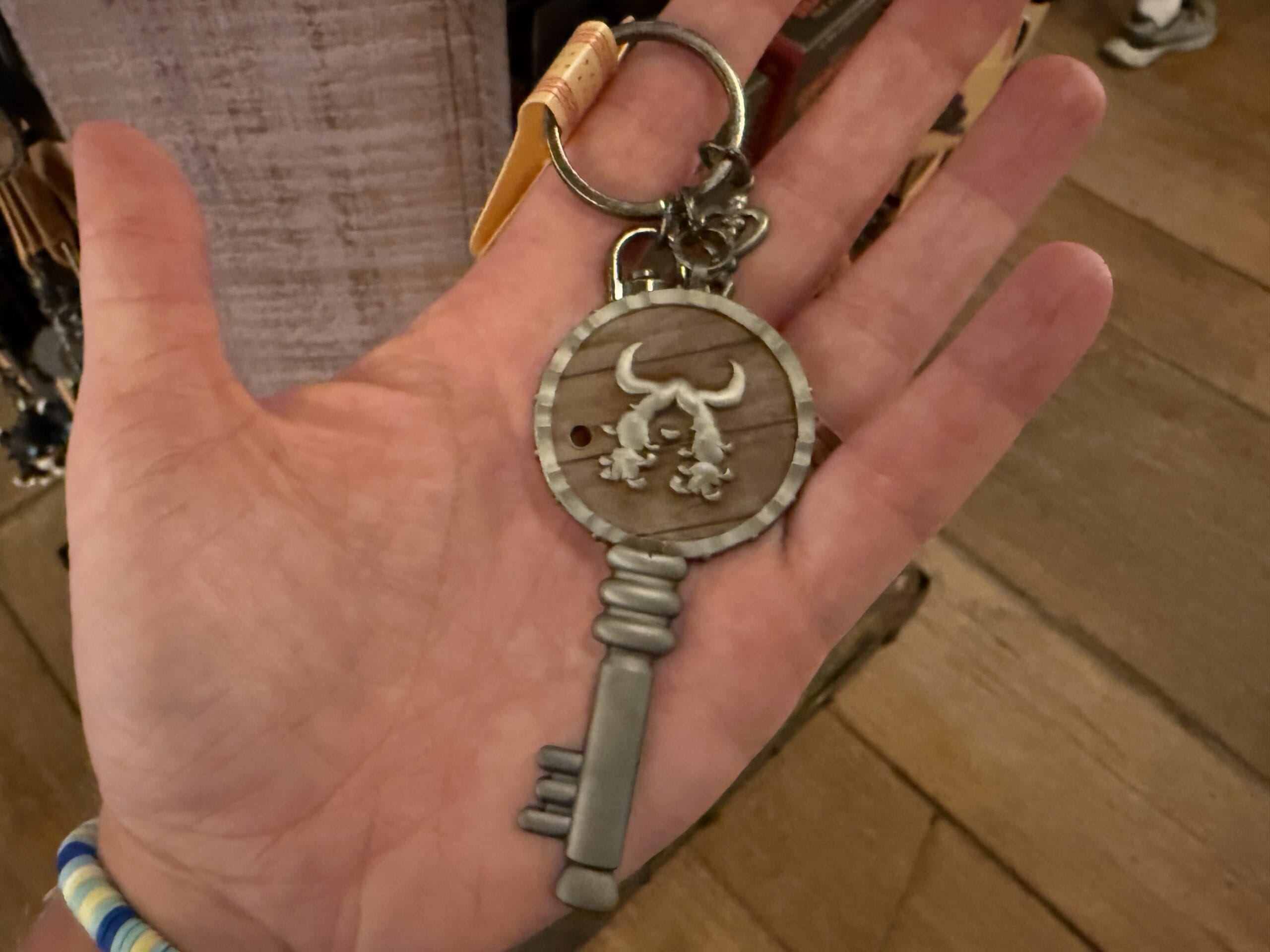 A hand holds a large, ornate metal keychain from Hiccup's Work Shop, featuring a bull’s head on the top.