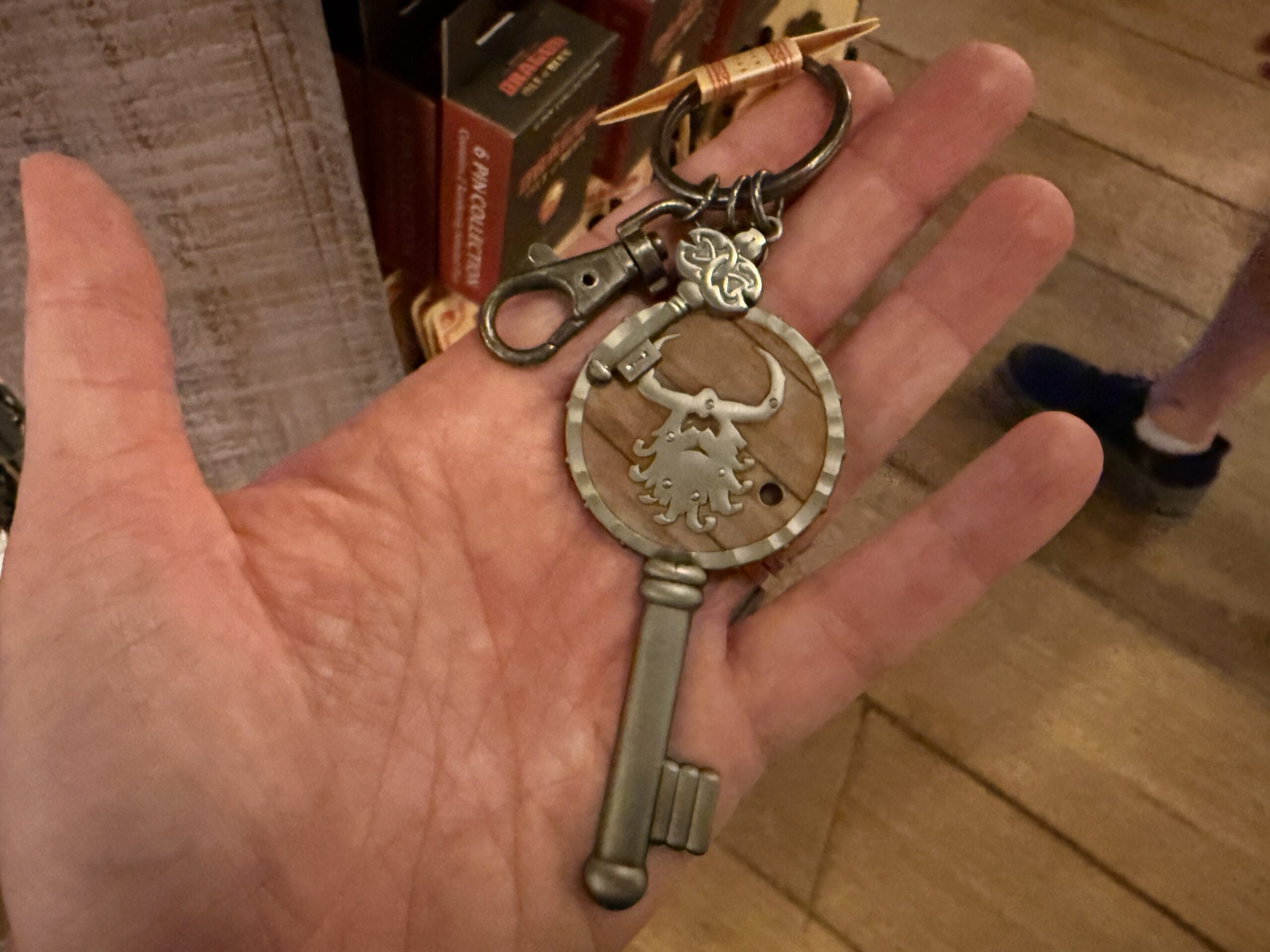 A hand holds a large, ornate key-shaped keychain from Hiccup's Work Shop with a bull design and metal clip attached.