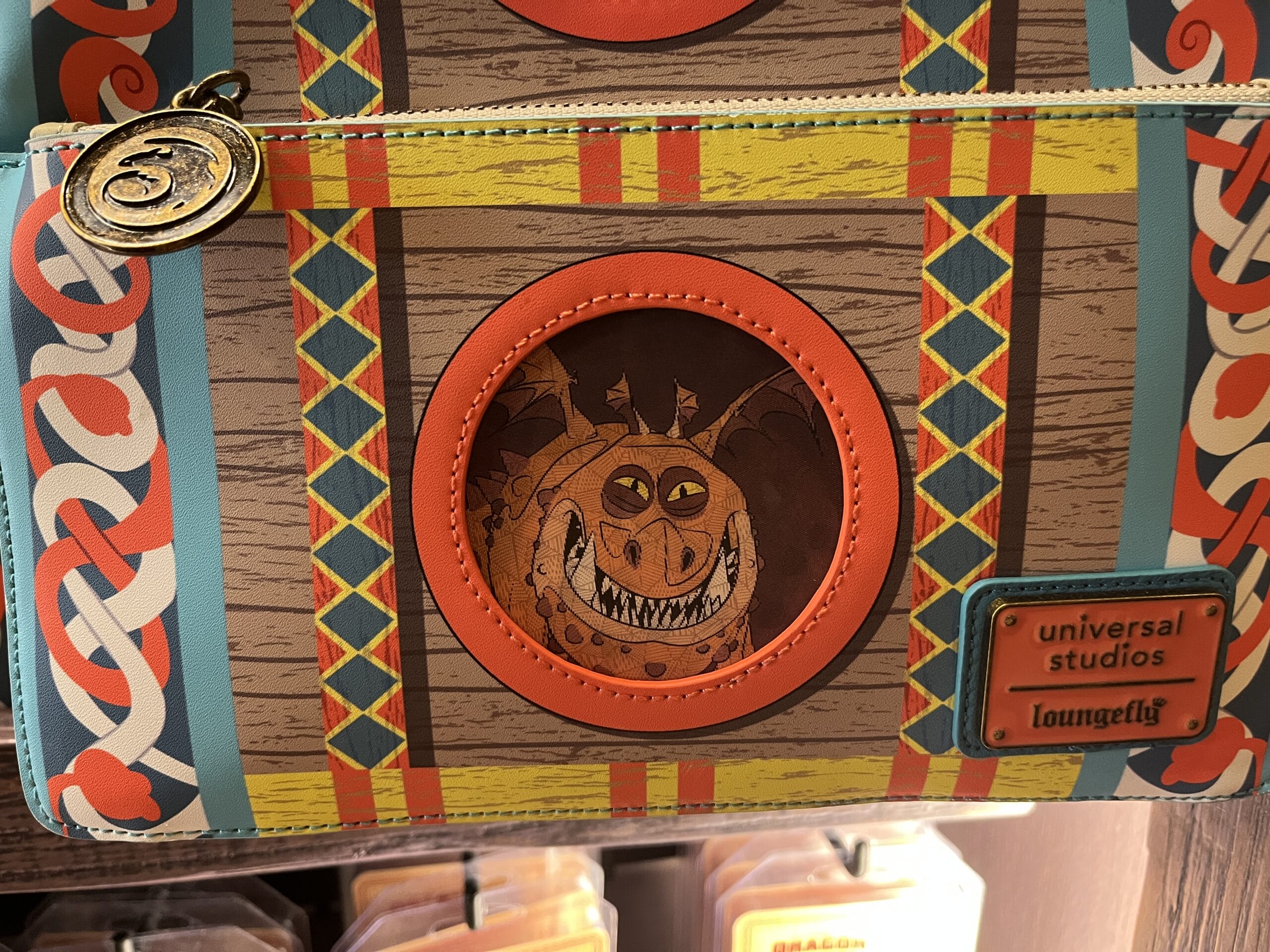 A bag with a grinning dragon illustration, Hiccup's Work Shop tag, Universal Studios, and Loungefly logo tags.