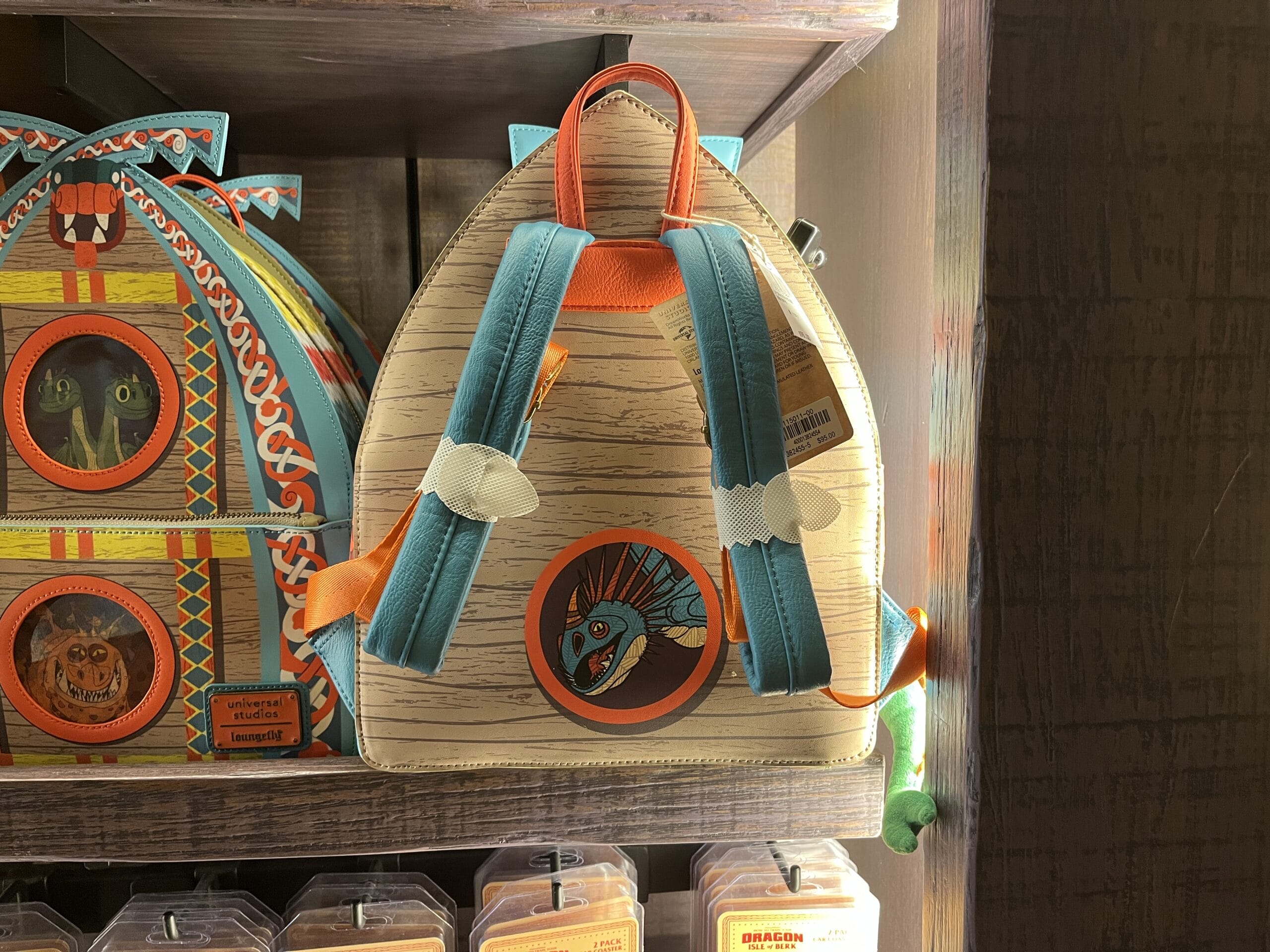 A backpack with a blue dragon design from Hiccup's Work Shop sits on a wooden shelf with other themed bags.