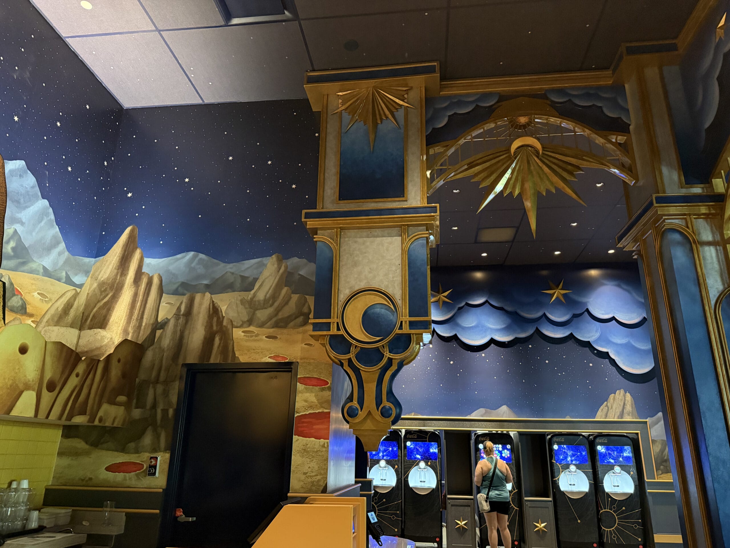 A person fills a water bottle at Celestial Park, surrounded by whimsical space murals in Epic Universe.