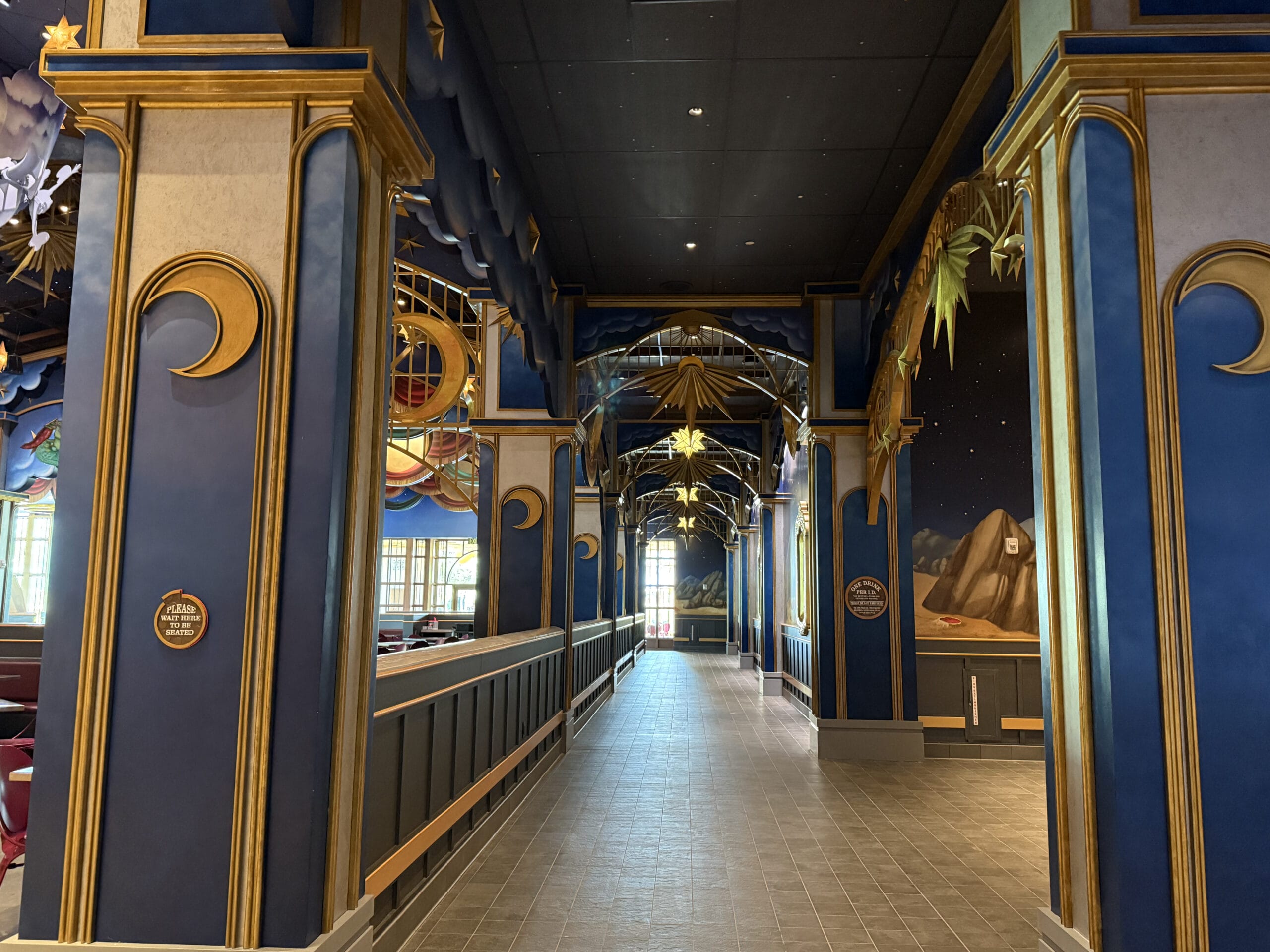 Hallway in Epic Universe’s Celestial Park with tall blue columns, gold accents, star decor, and cloud murals.