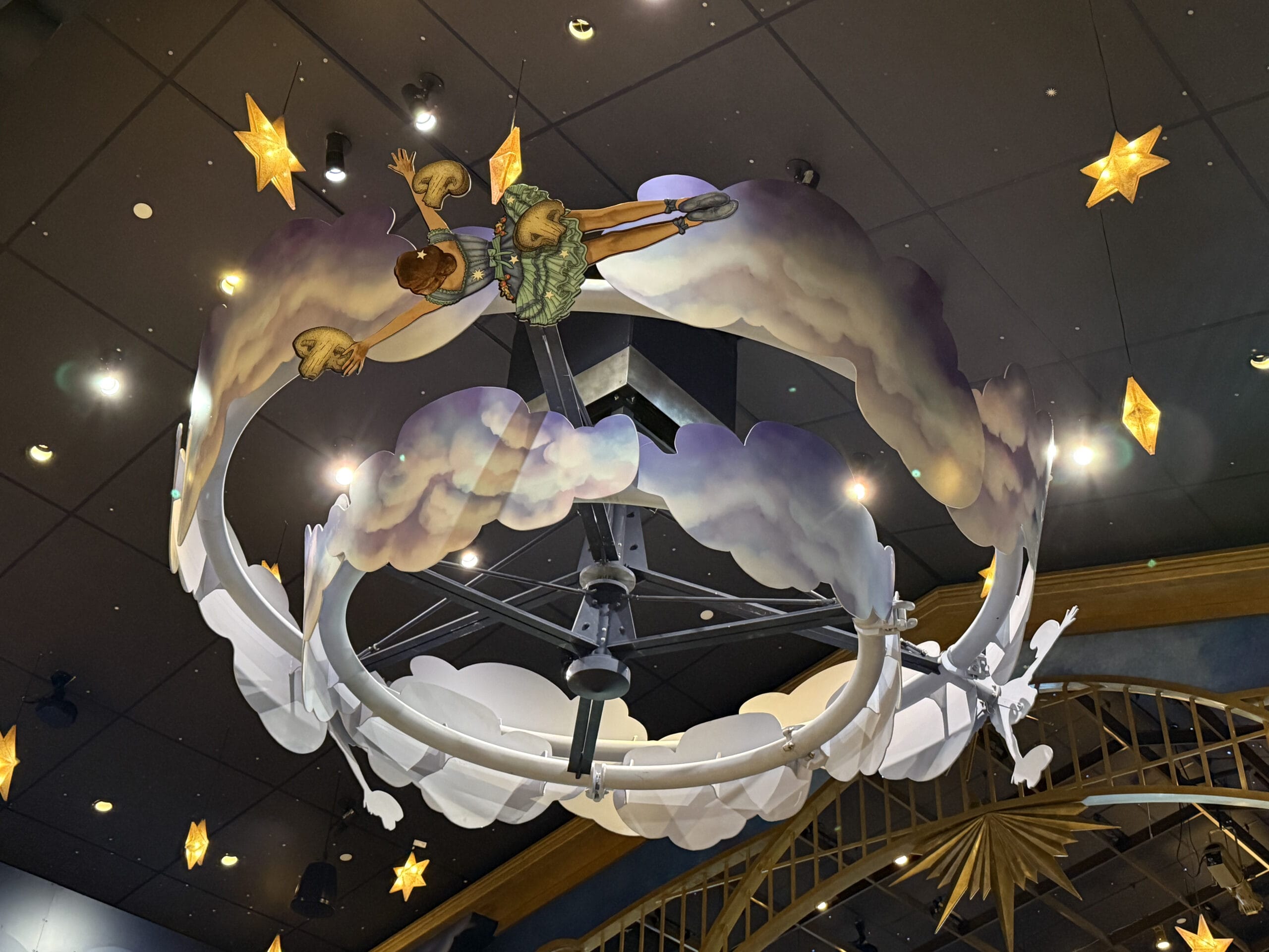 A whimsical ceiling display at Pizza Moon Restaurant shows a child riding clouds, with stars and an Epic Universe backdrop.